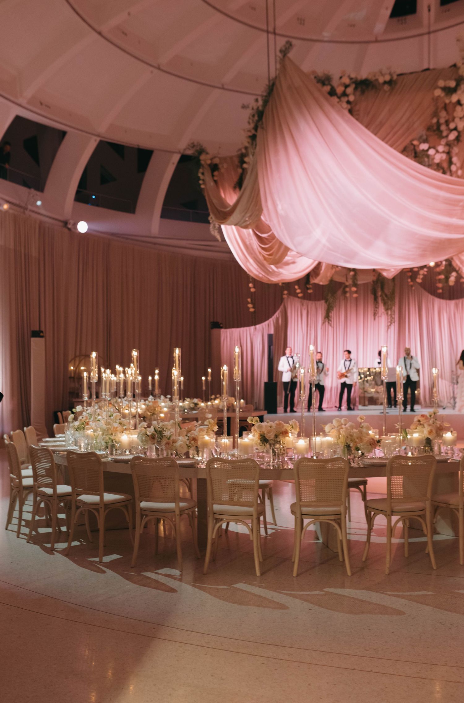 Luxurious wedding reception hall decorated with pink drapes and white table settings under soft lighting.