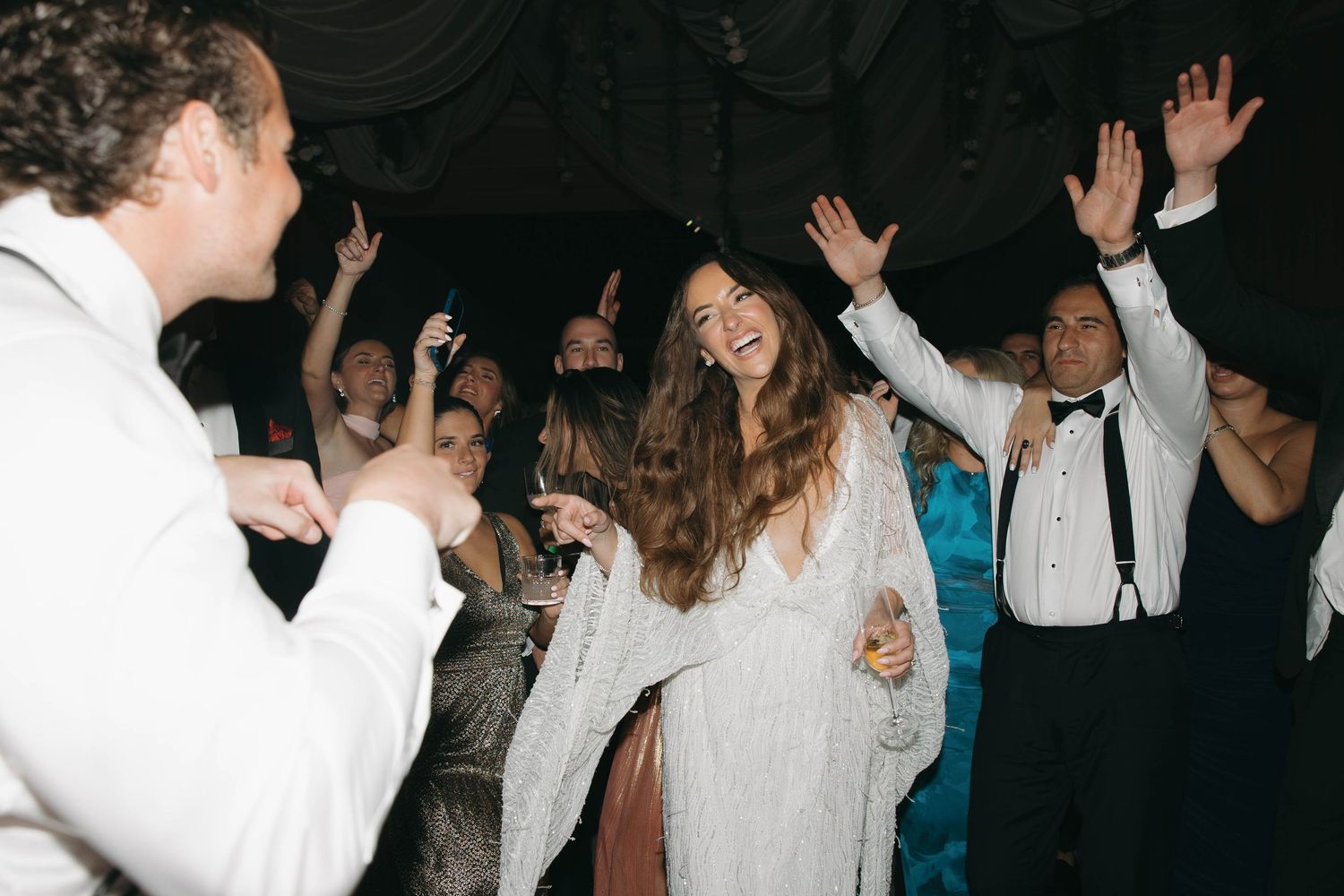 Wedding party dancing and celebrating on darkened dance floor with dramatic lighting.