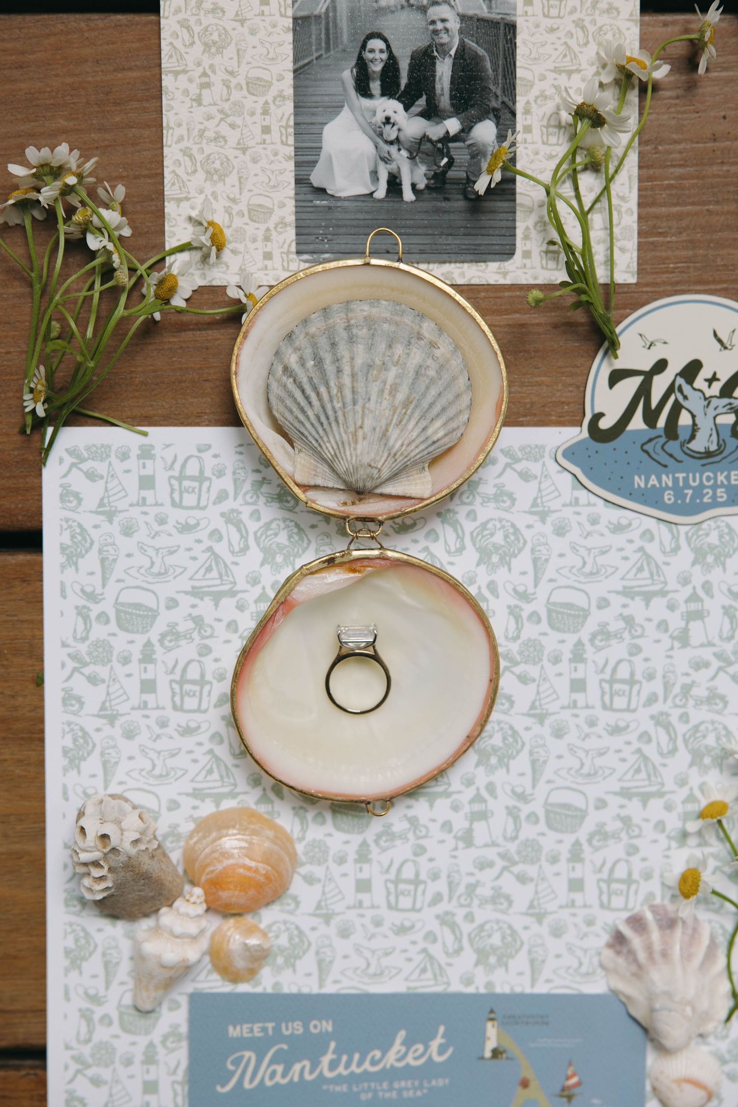 Wedding ring displayed in embroidery hoop with seashells and Nantucket-themed decor on wooden surface.