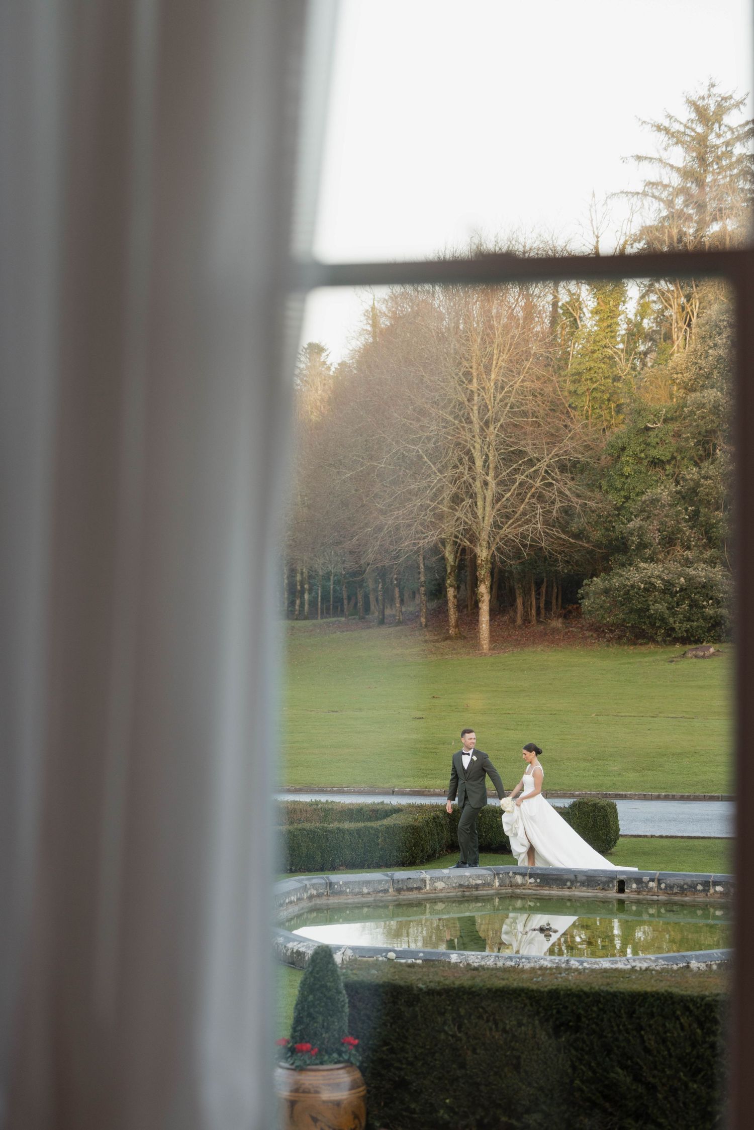 Wedding photo session viewed through window panes overlooking a landscaped garden.
