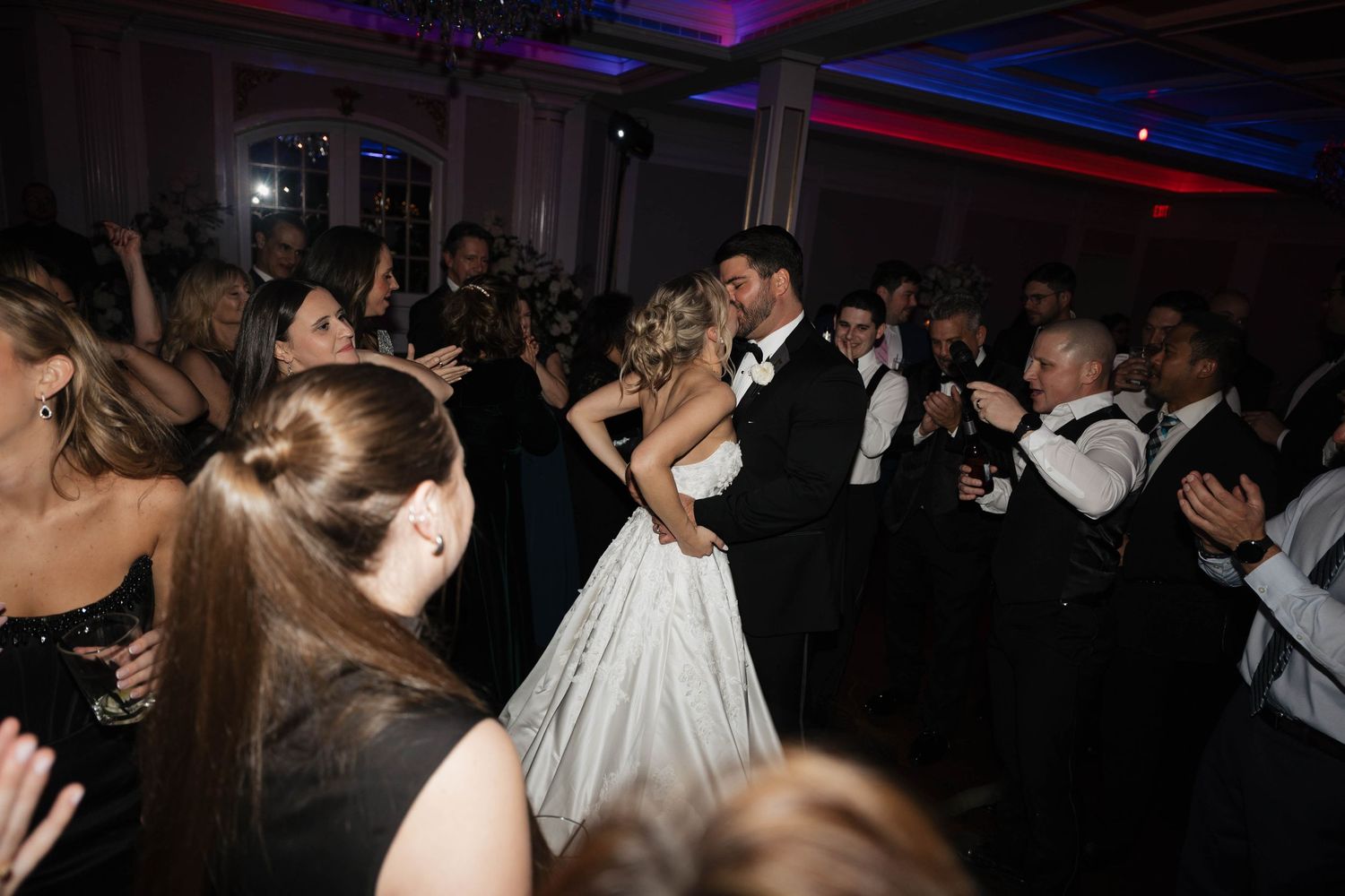 Couples dancing at an elegant wedding reception with dramatic purple and red lighting.
