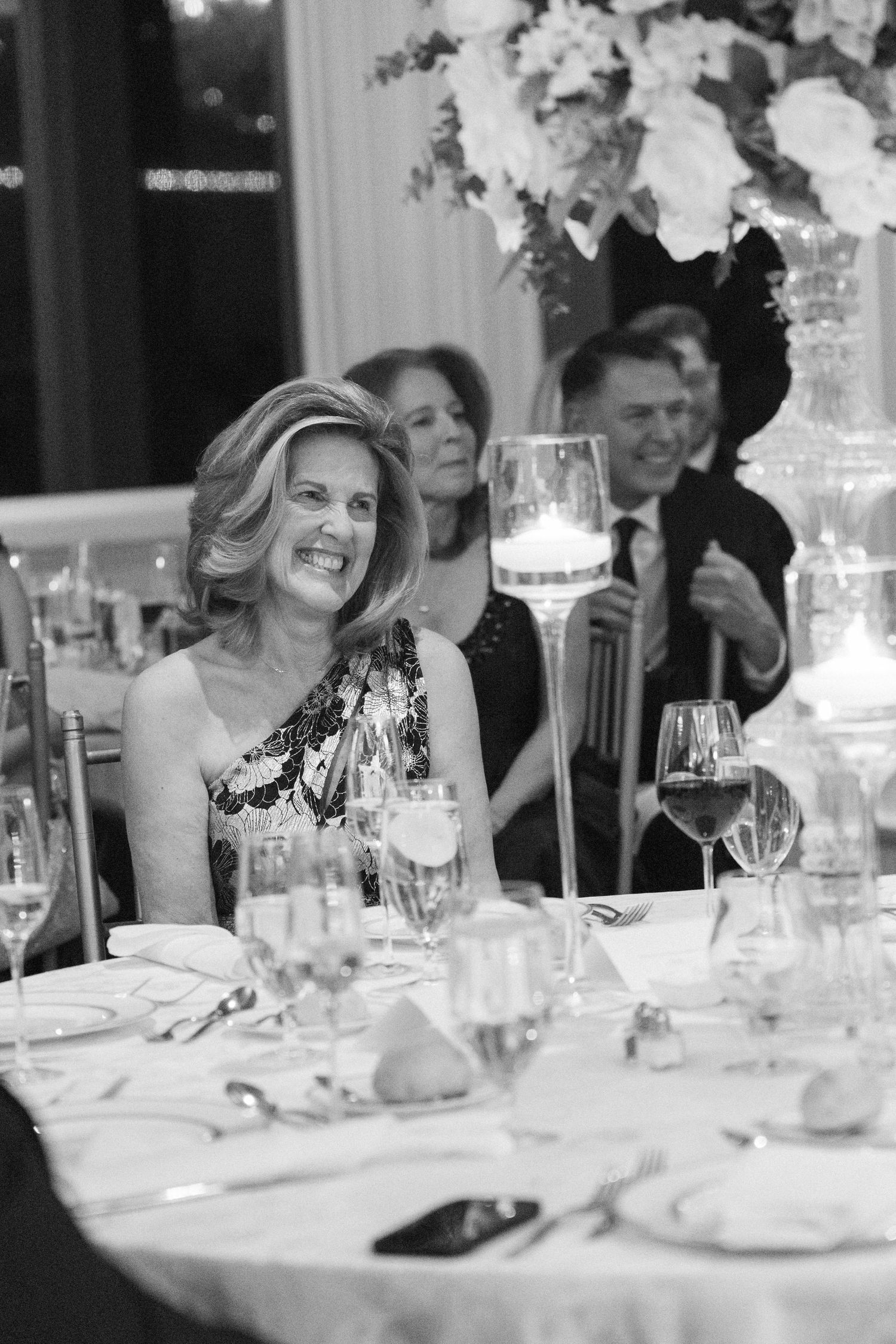 Wedding guest in formal attire laughing during an elegant dinner reception.