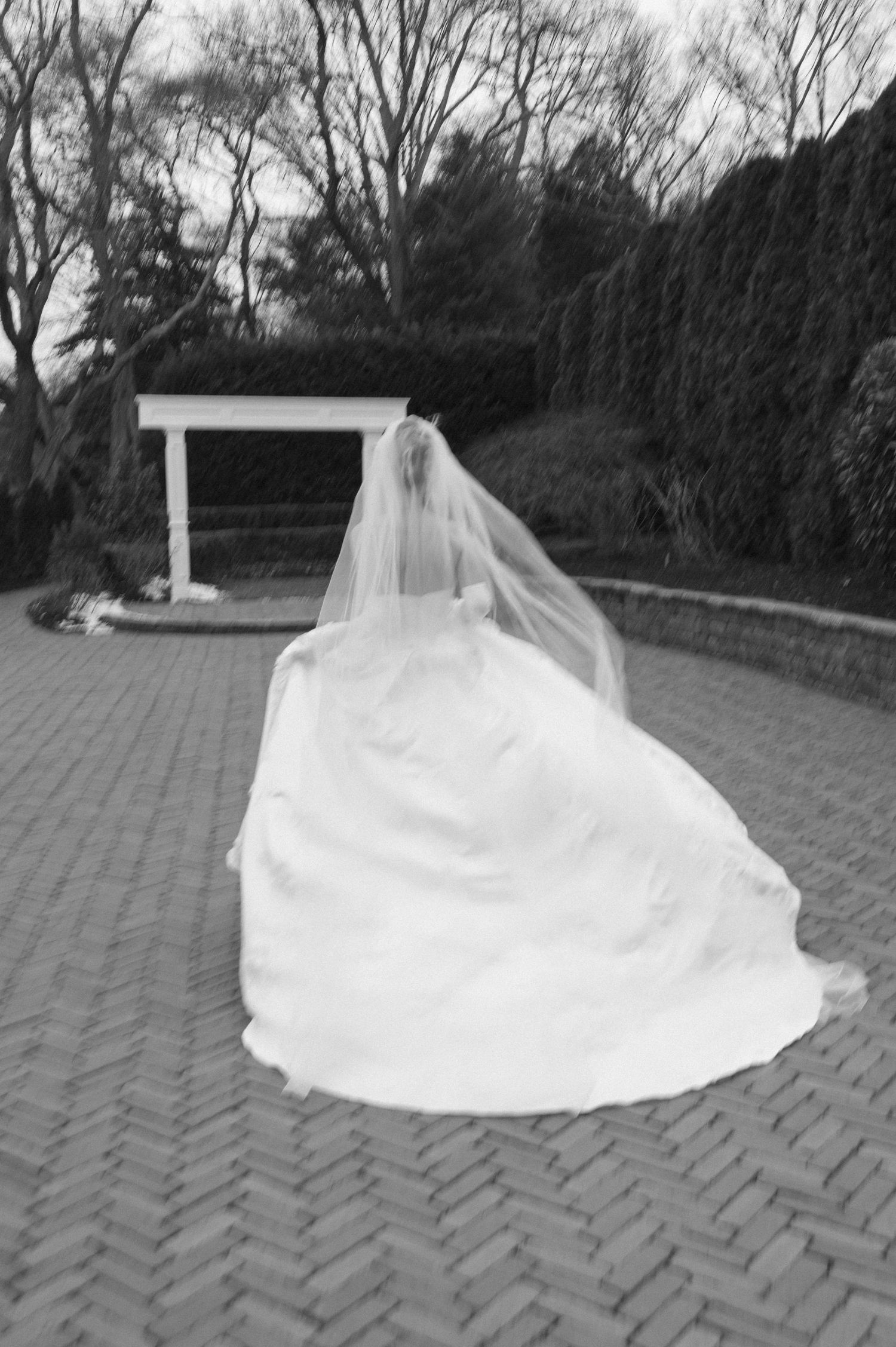A wedding dress and veil create an artistic silhouette against a brick paved courtyard.