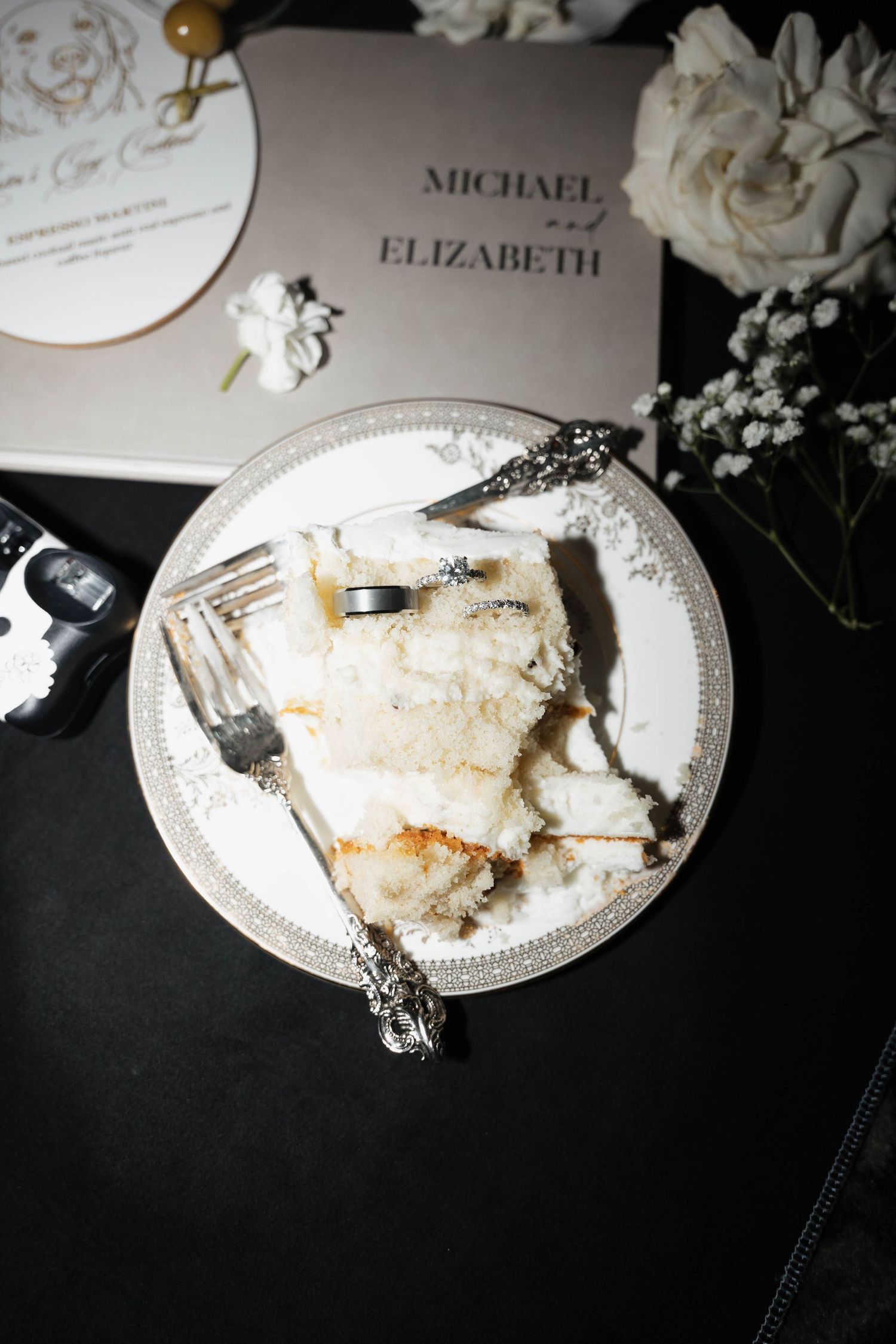 Partially eaten wedding cake on ornate white plate with name cards visible.