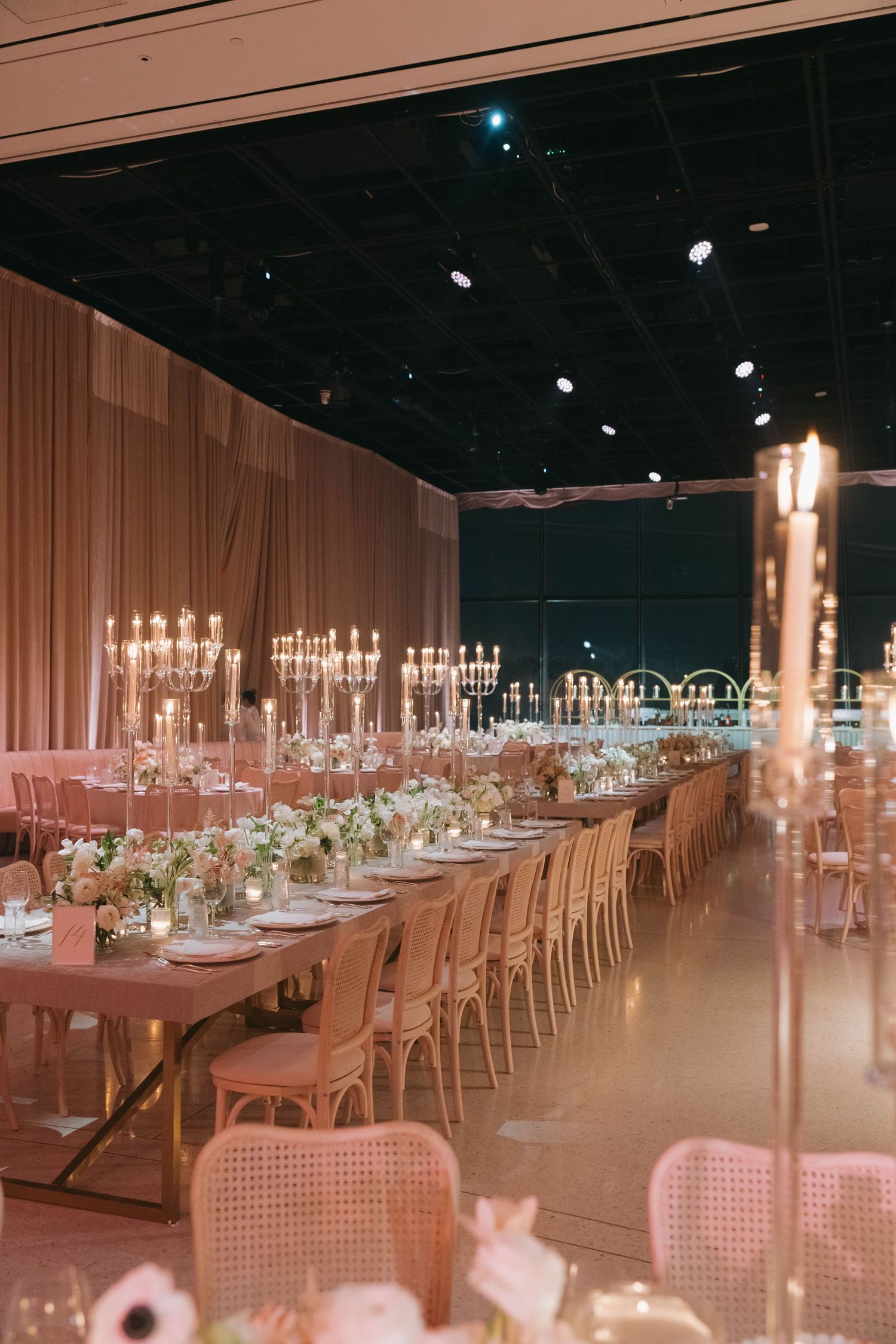 Spacious reception venue with cane-back chairs and elegant table settings under dramatic lighting.