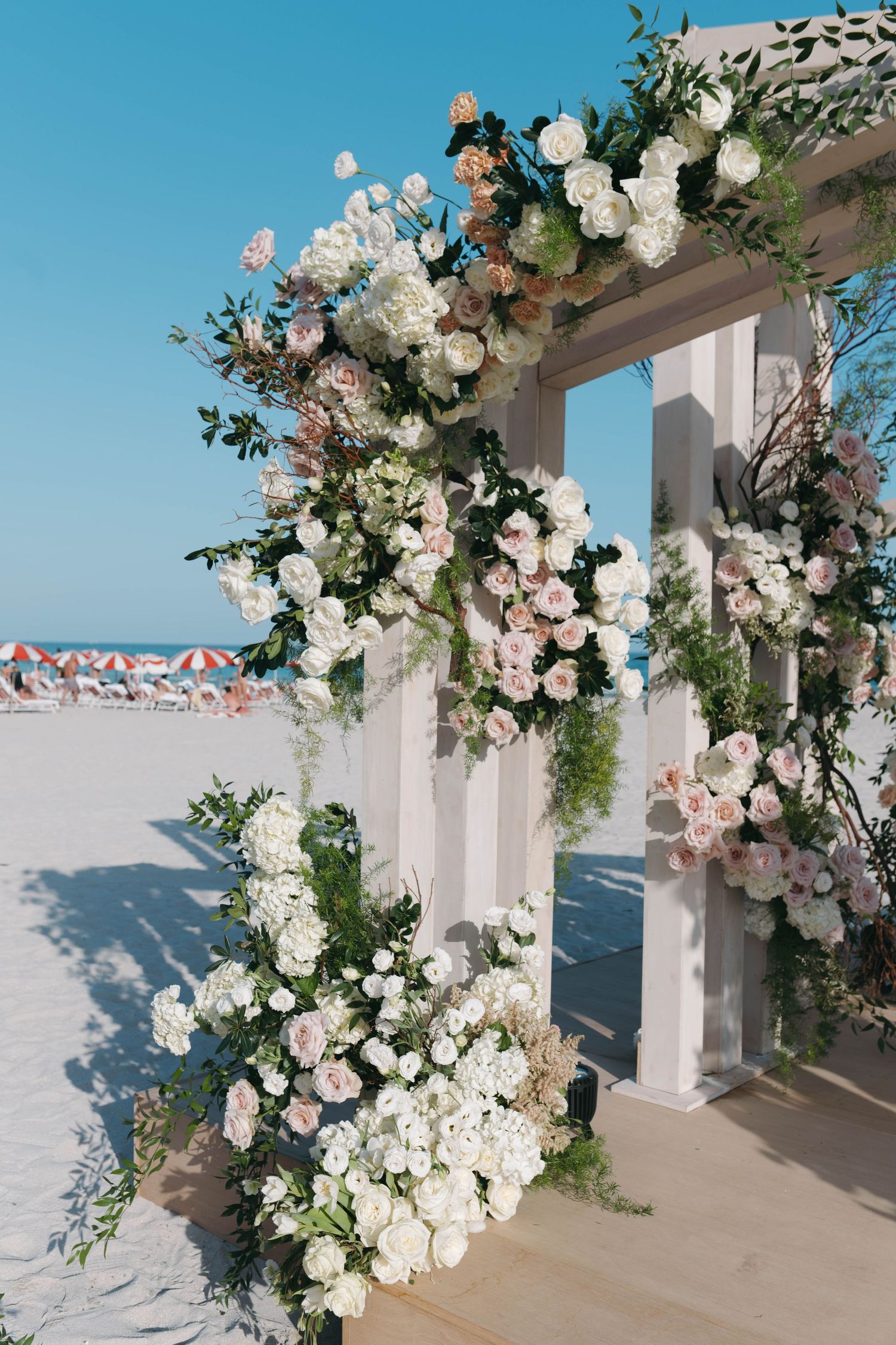 Lush floral arrangements with white and pink blooms decorating a beachside wedding structure.