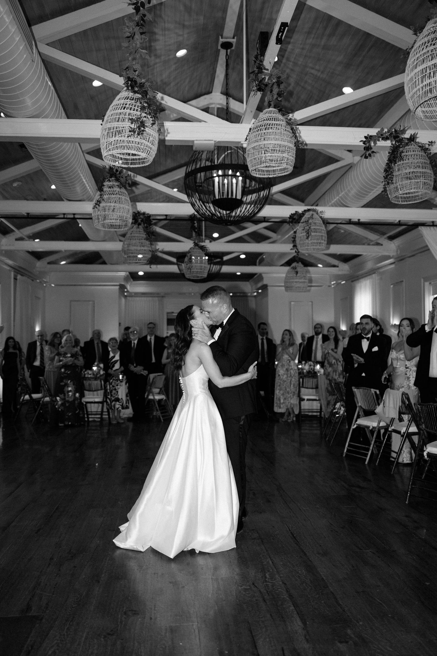 Wedding dance in a reception hall with hanging wicker lanterns and hardwood floors.