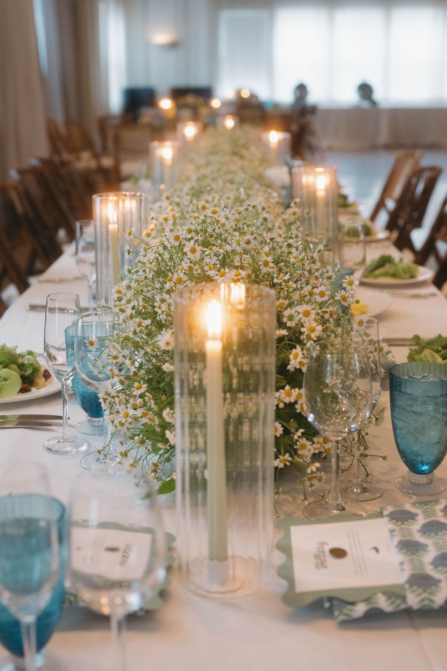 Wedding table centerpieces featuring glass candle holders and baby's breath flowers with blue glassware accents.