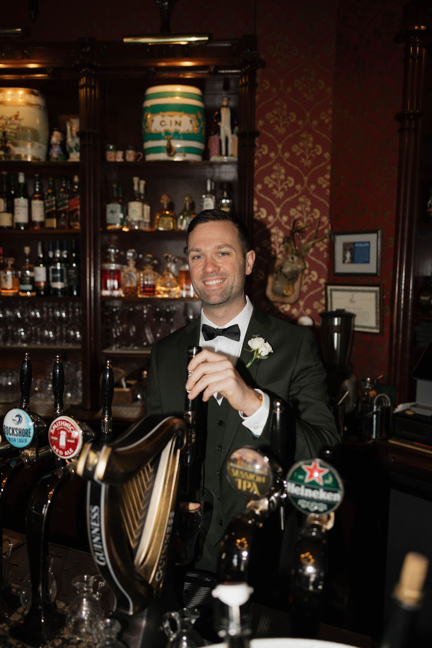 Bartender in formal attire serving drinks at an elegant bar with vintage decor.