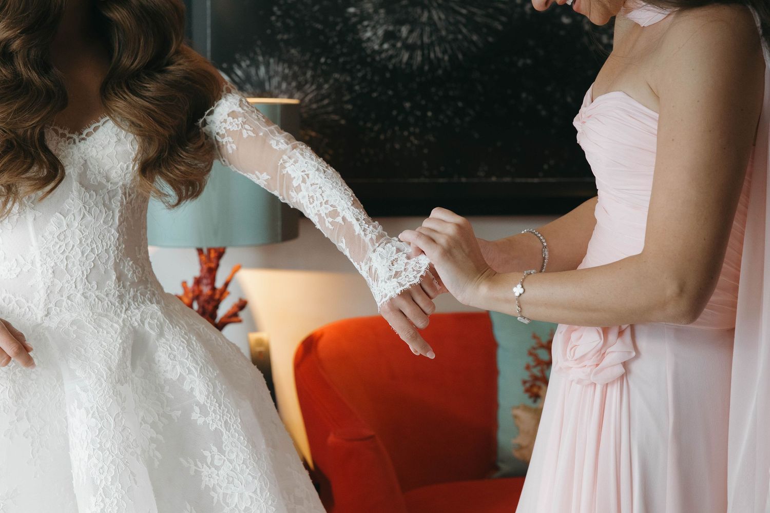 A bride in a white lace gown gets help with final preparations before her wedding ceremony.