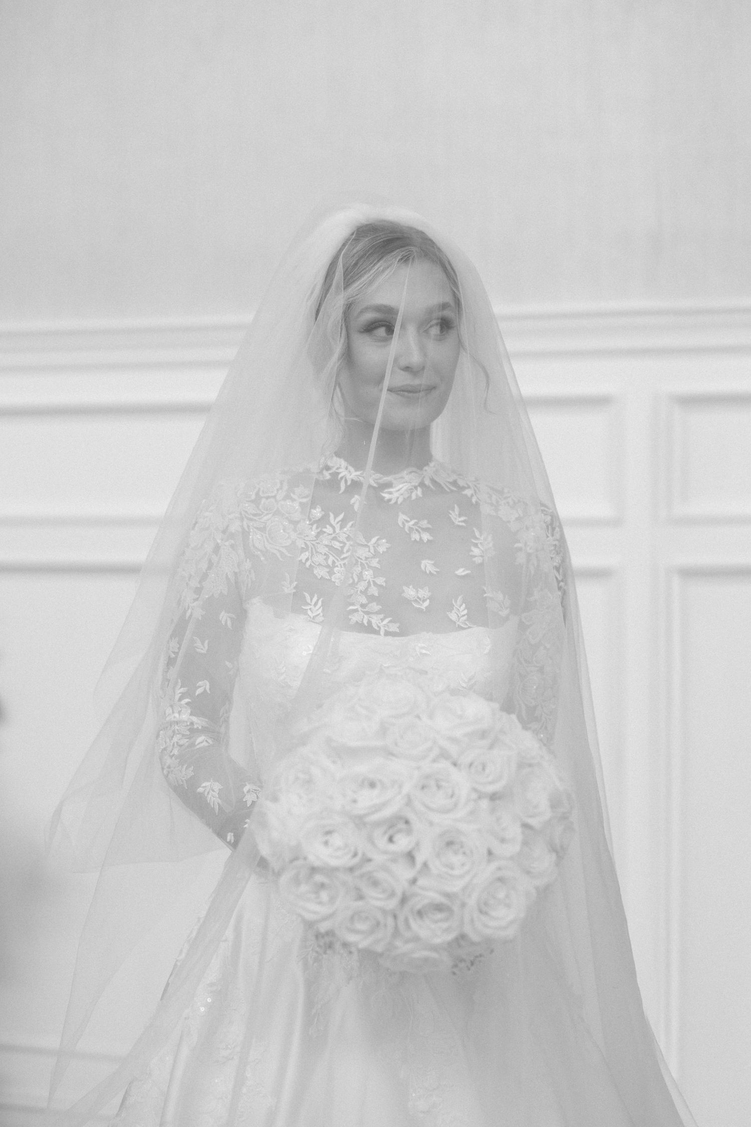Close-up of bride holding white rose bouquet with delicate lace veil details.