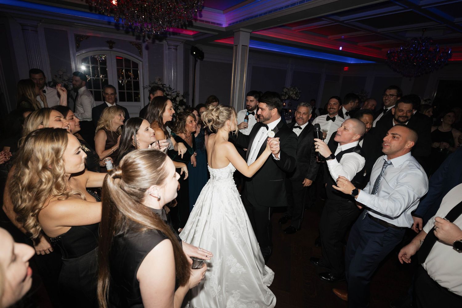 Wedding reception dance floor filled with guests celebrating under purple and blue lighting.