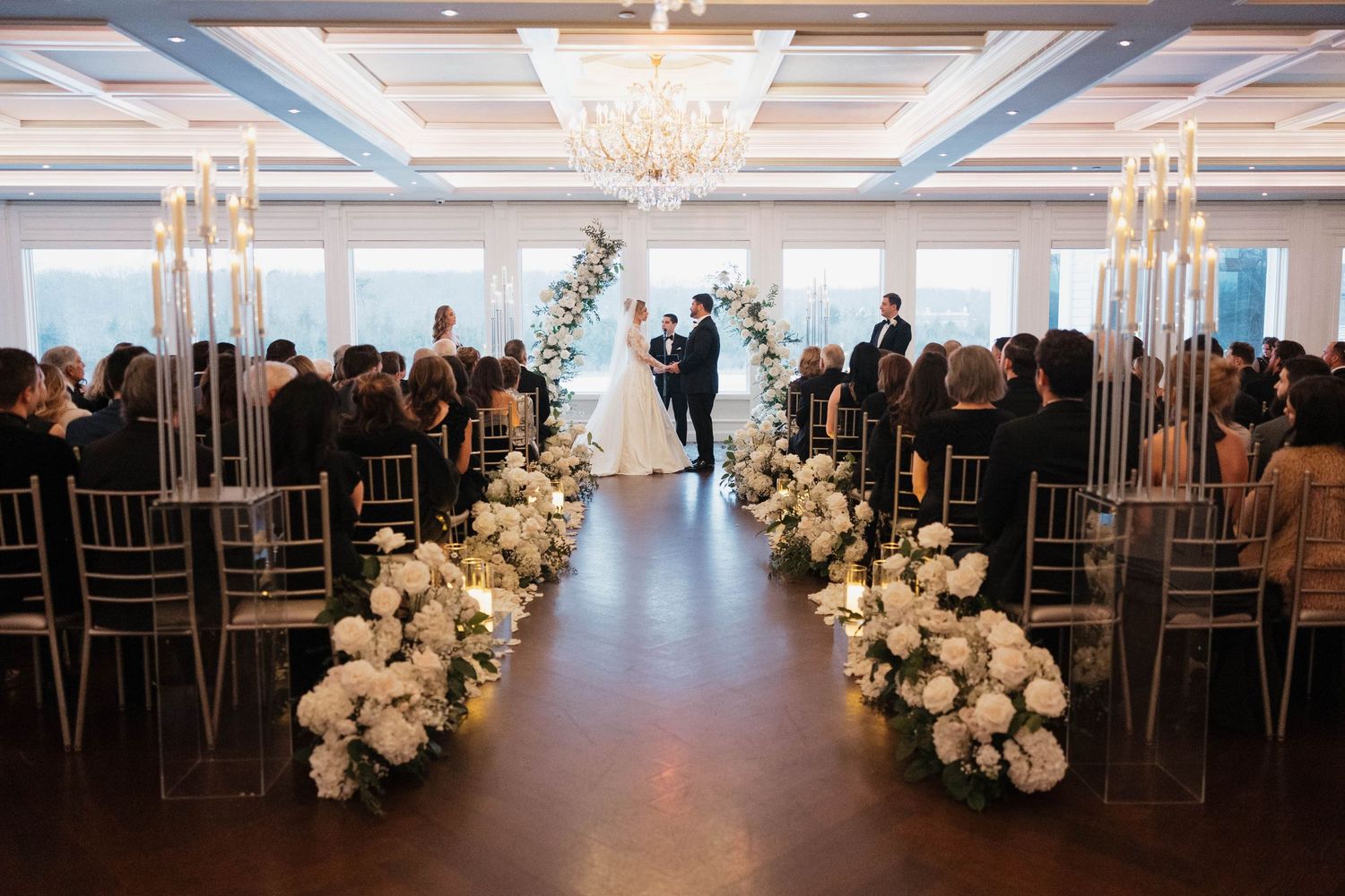 Elegant ballroom wedding venue with crystal chandeliers and rows of gold chairs.