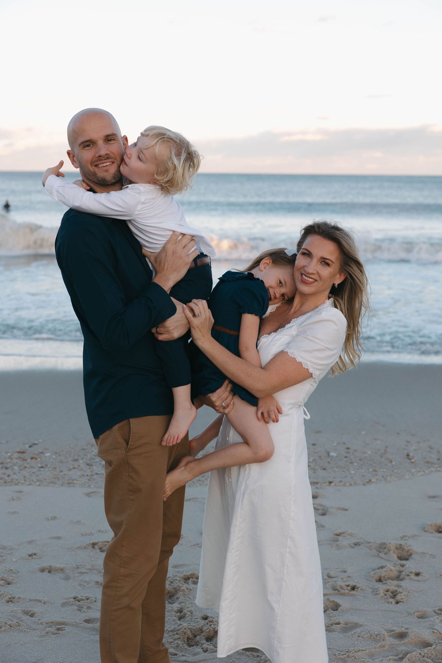 A playful family moment captured at sunset on the beach as they embrace and laugh together.