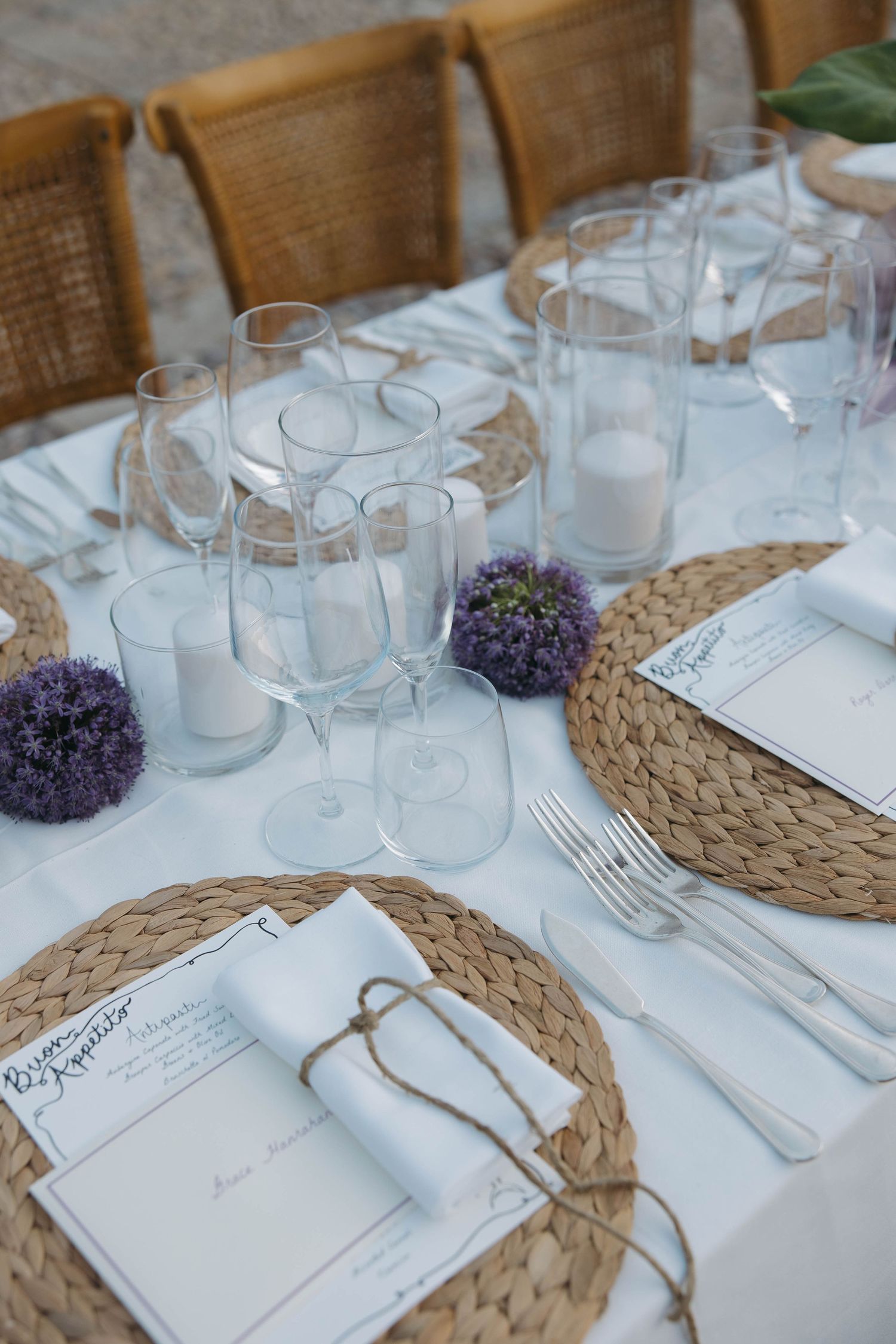 Elegant table settings with woven chargers, white menus, and purple floral accents.