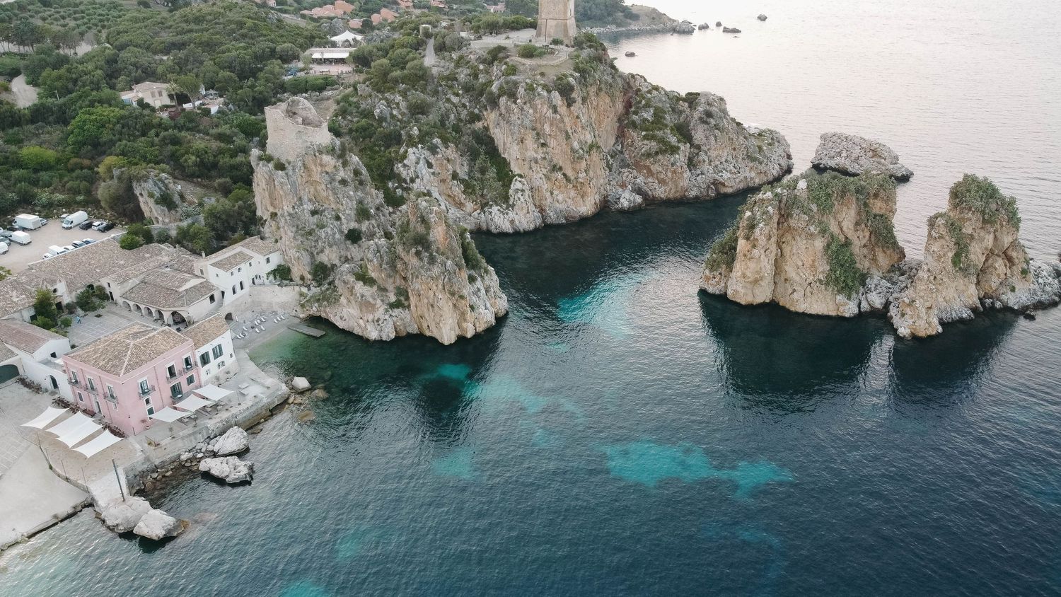 Aerial panorama of a rocky Mediterranean coastline with turquoise waters and white buildings nestled against cliffs.