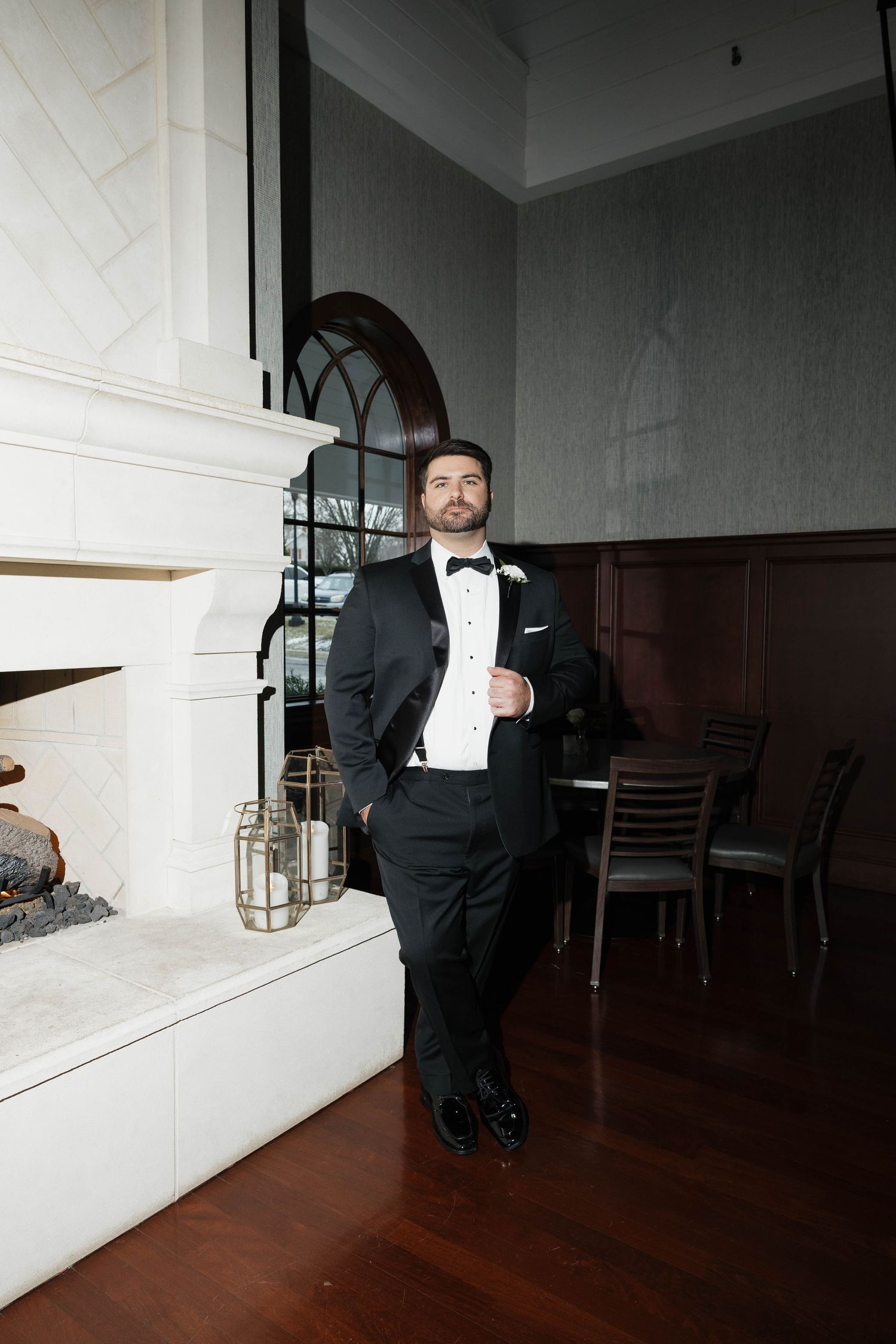 A formal black tuxedo with bow tie against an elegant white fireplace backdrop.
