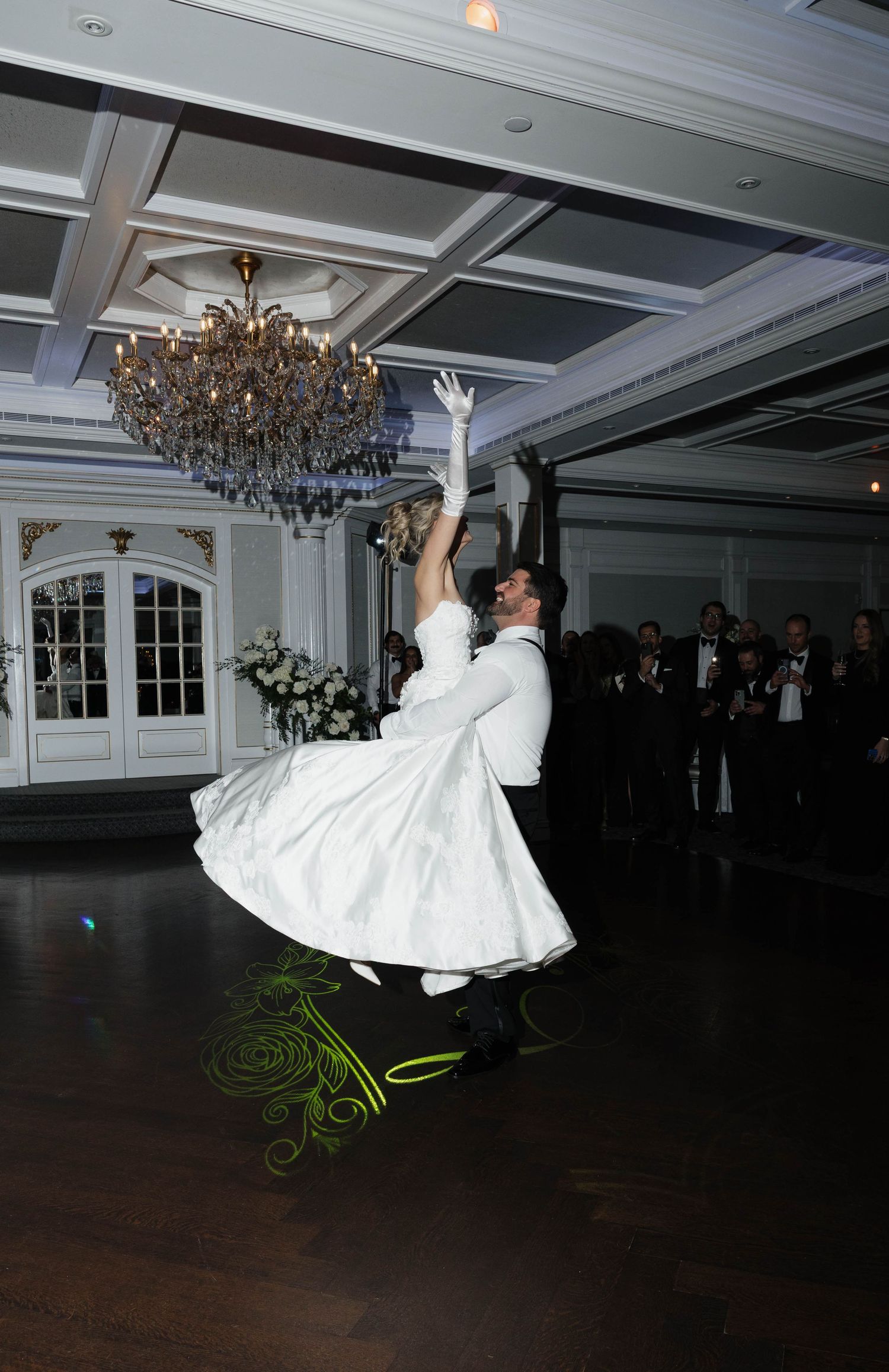 Dramatic dance lift performance on dark ballroom floor under crystal chandelier.