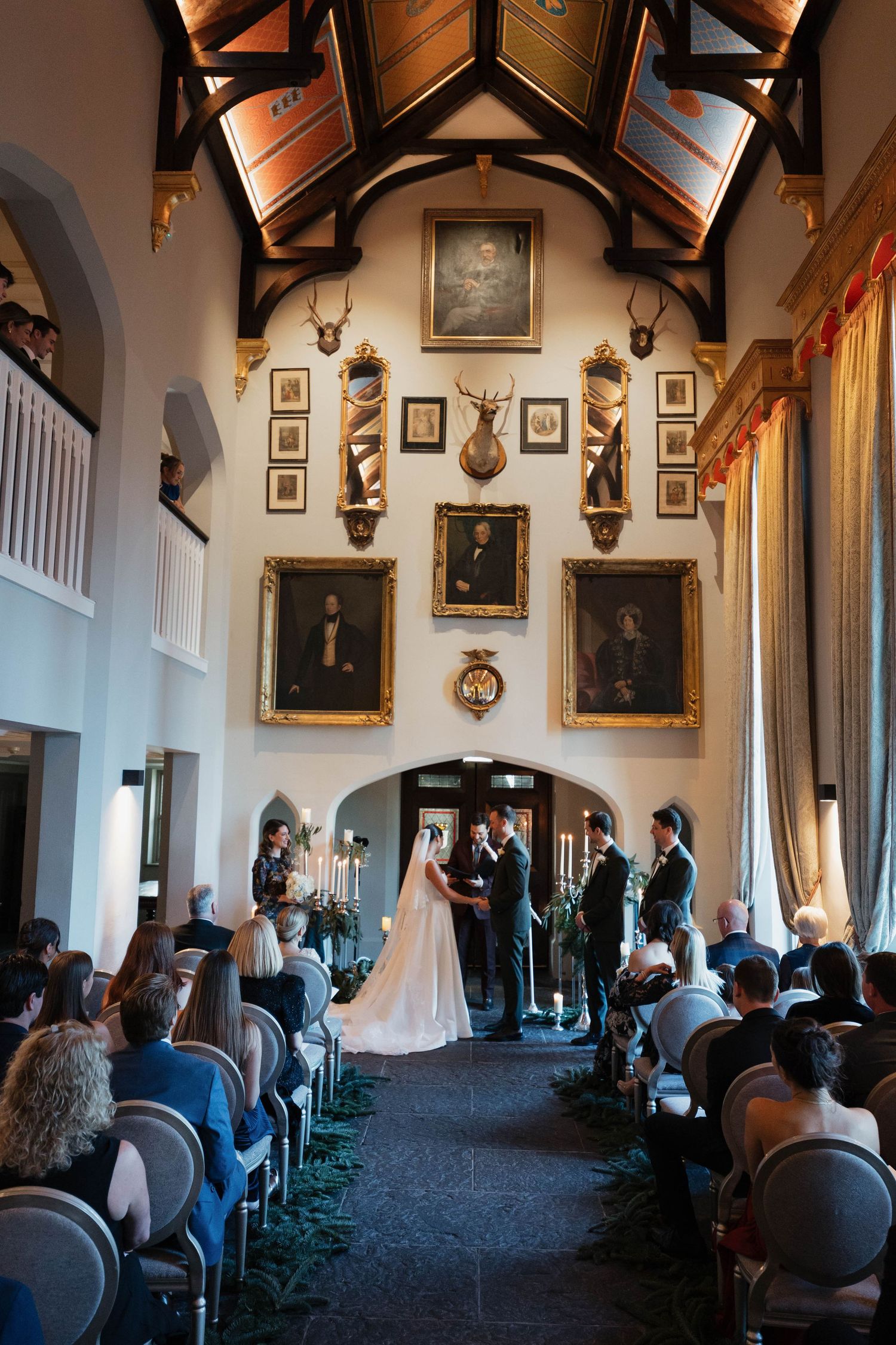 Historic great hall with wooden beamed ceiling, portrait-lined walls, and elegant seating arrangements.