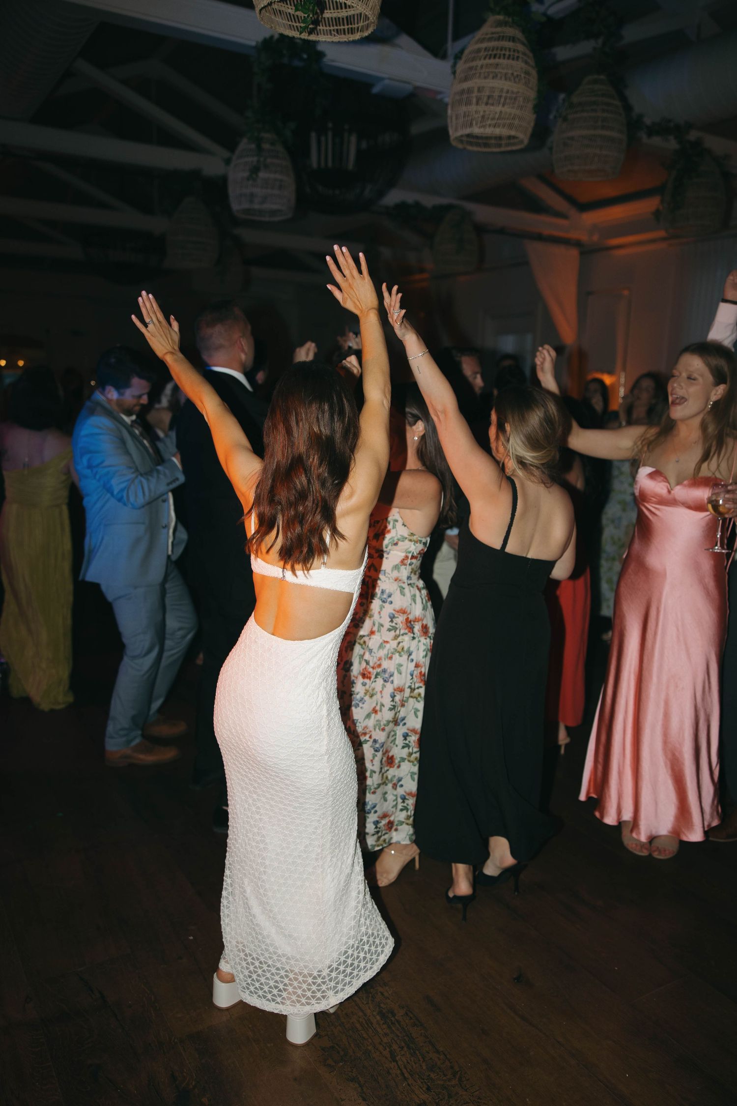 Wedding guests dancing with raised arms under hanging lantern decorations.