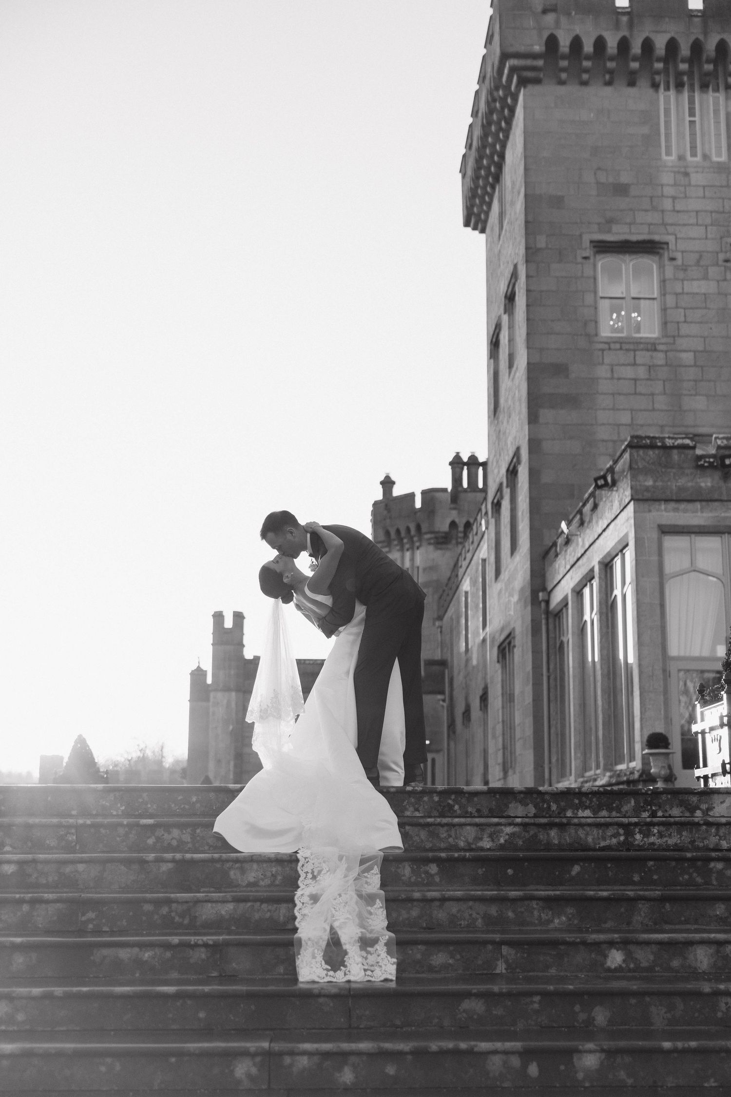 Romantic wedding couple embraces on stone steps of a castle at sunset.