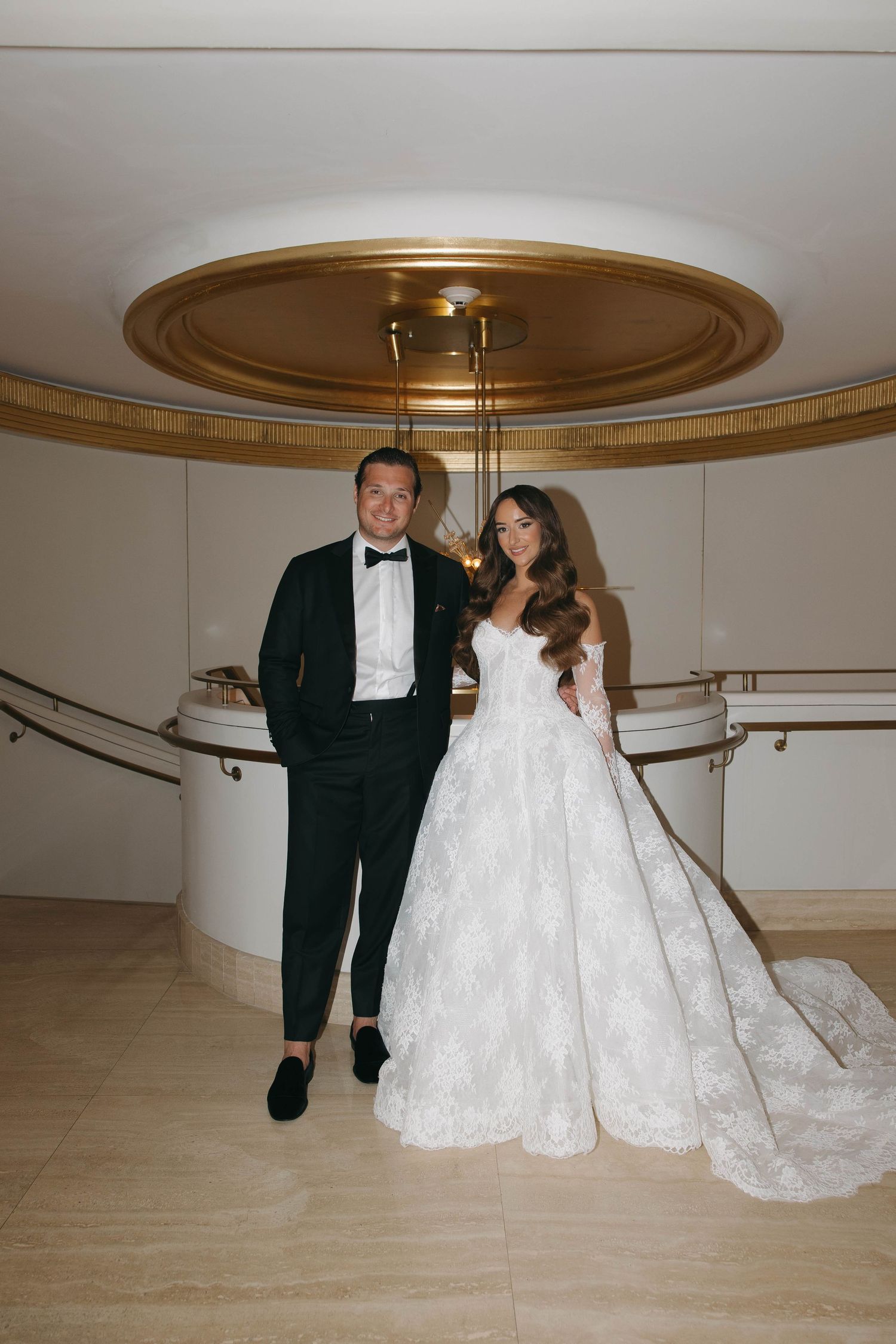 Wedding couple walking through an elegant hallway with golden ceiling details.