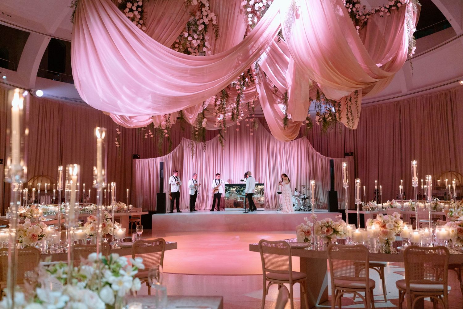 Wedding reception hall with pink fabric draping and crystal chandeliers creating a romantic atmosphere.