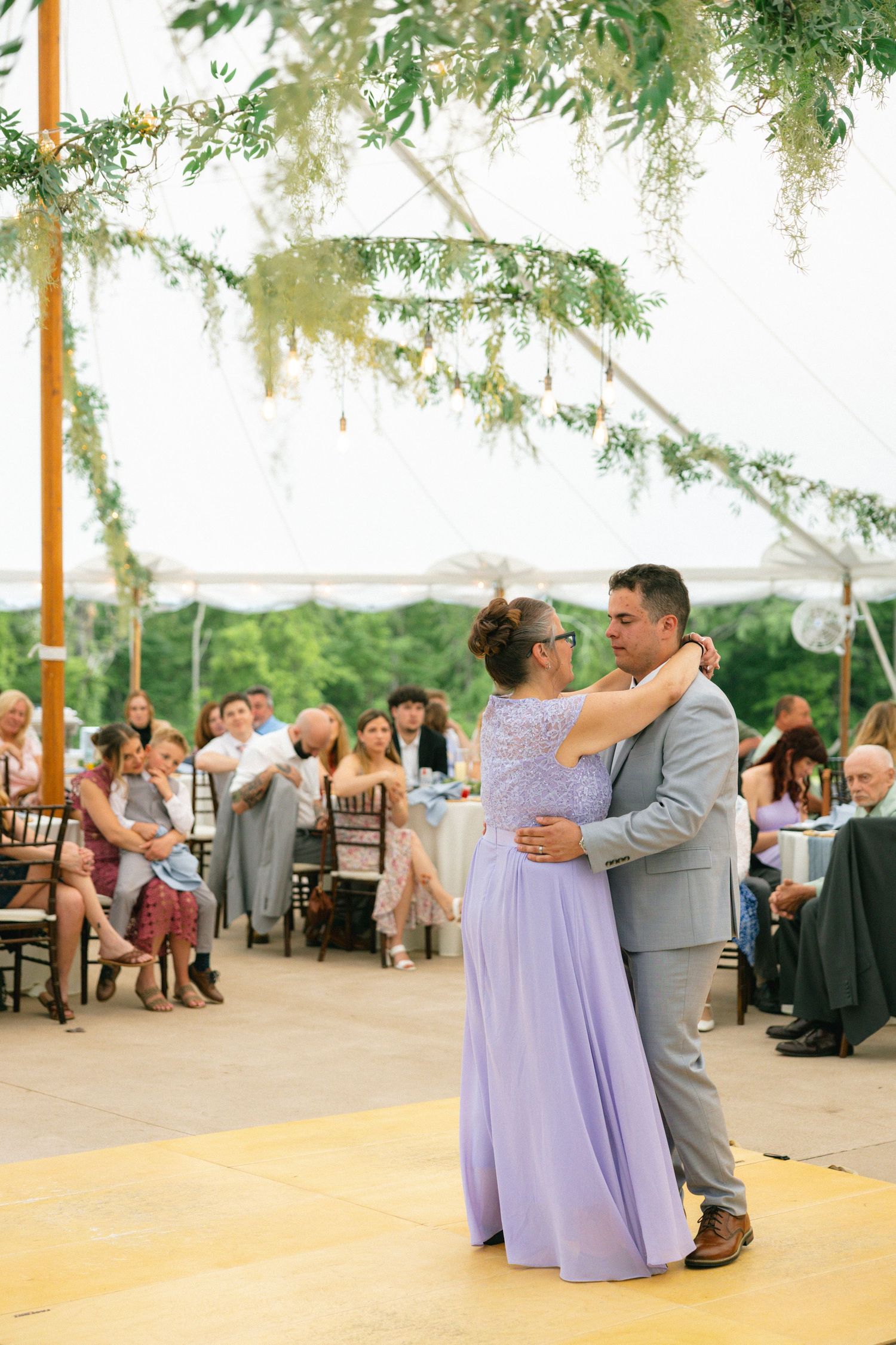 A mother and son share a tender dance at an elegant outdoor wedding reception under a floral canopy.