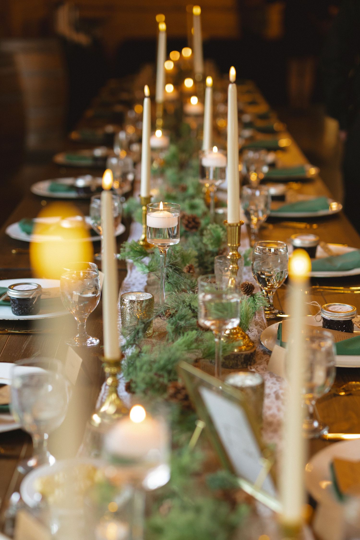 Elegant table setting with white taper candles, greenery garland, and place settings for a formal holiday dinner.