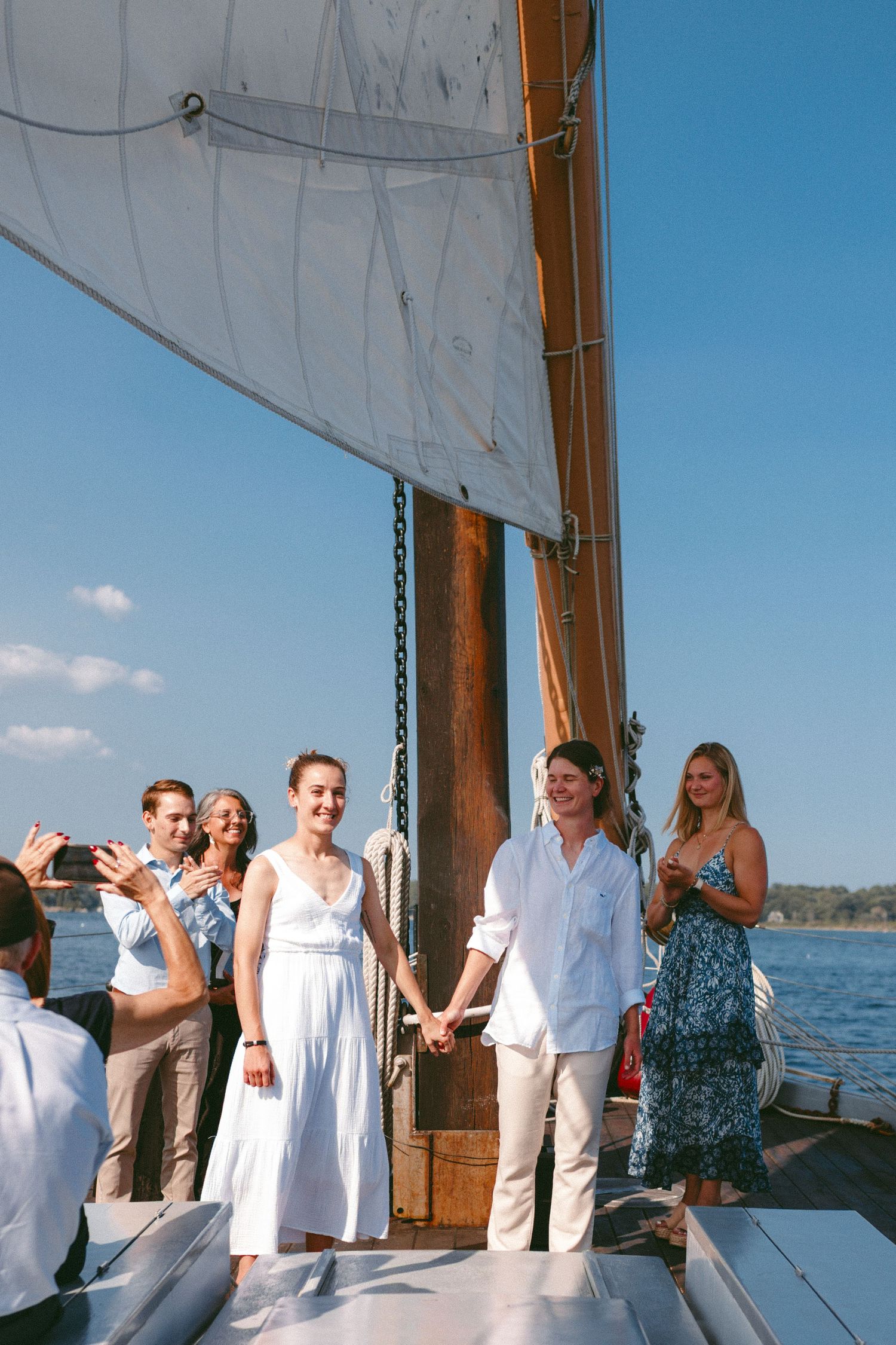 Wedding celebration on a sailboat deck with guests cheering against nautical backdrop.