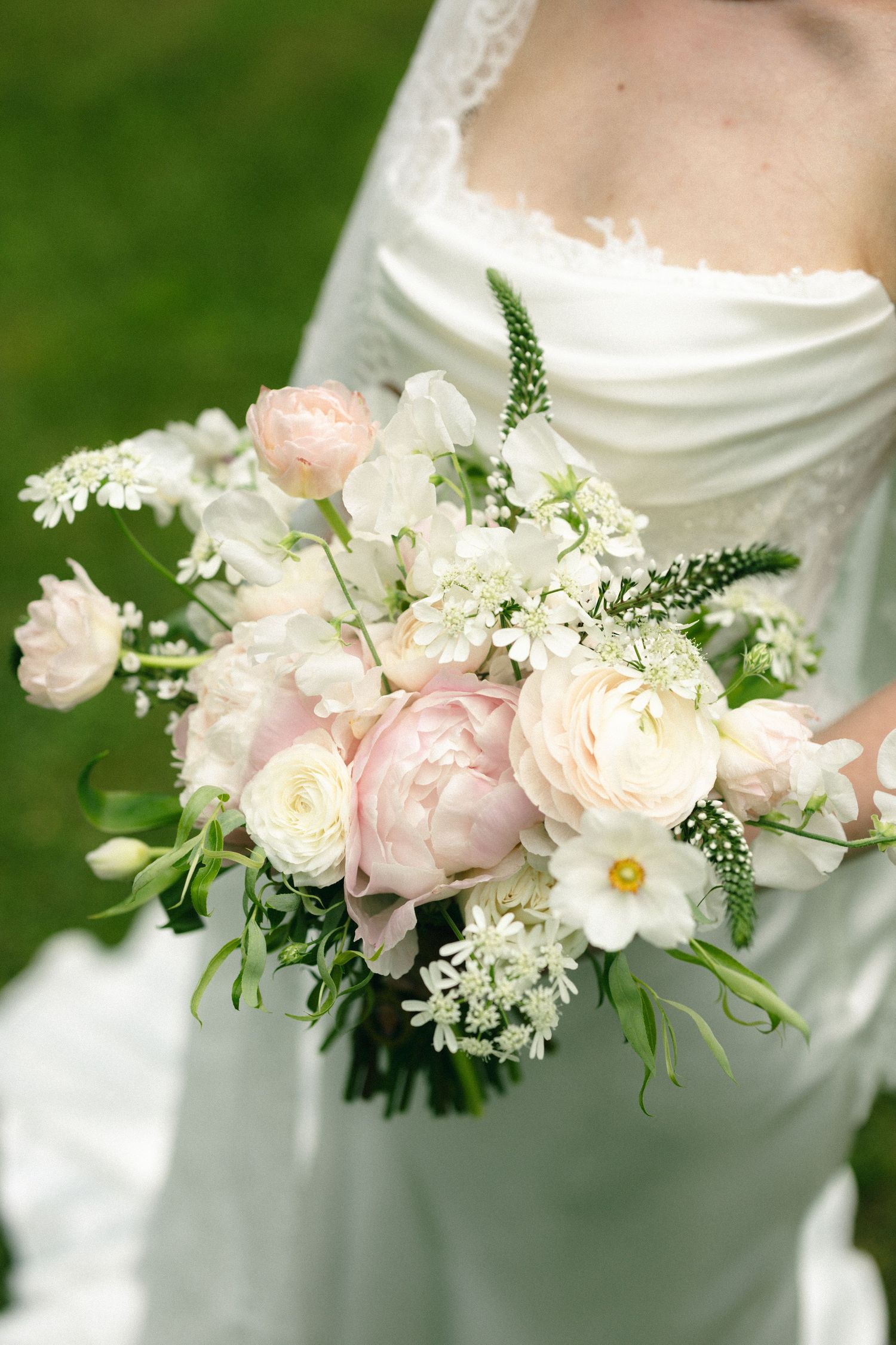 Bride holds a romantic bouquet of blush peonies and white flowers against her white wedding gown.
