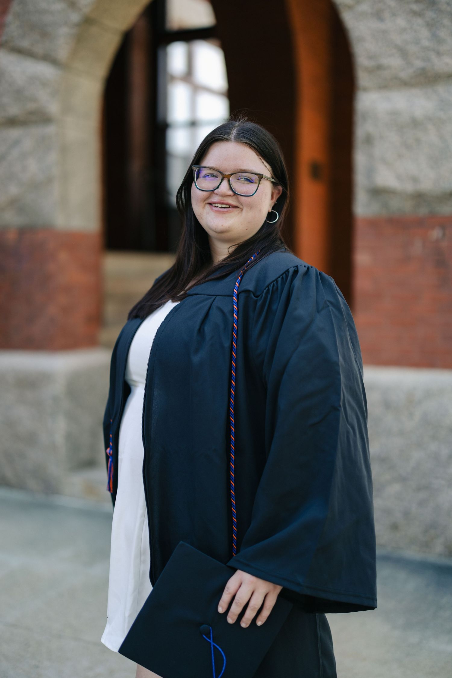 Graduate in academic regalia poses in front of stone building.