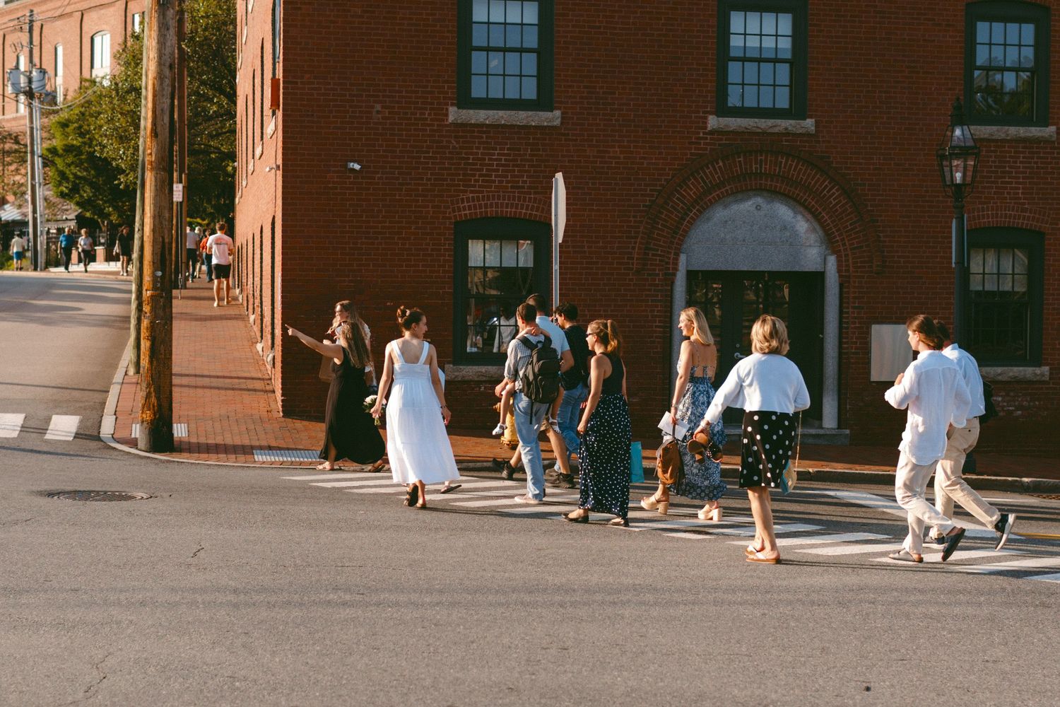 Wedding party walking along a historic brick building with large windows.