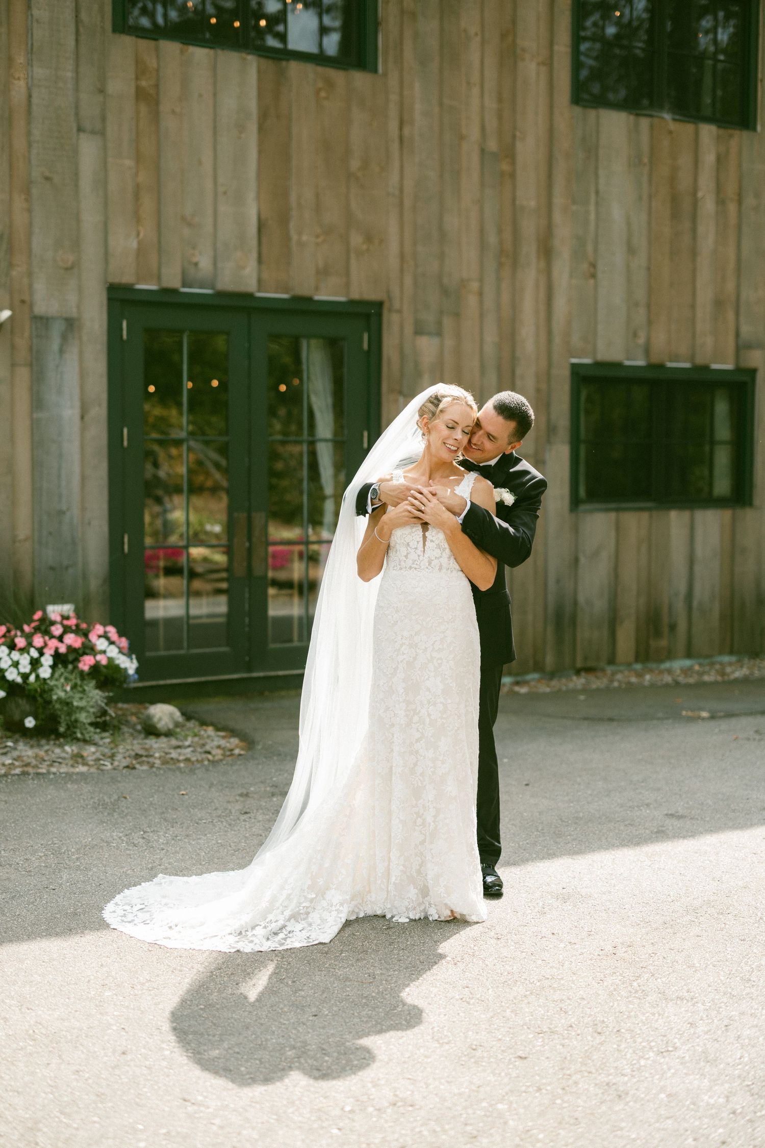 A romantic wedding couple embracing outside a rustic barn venue.