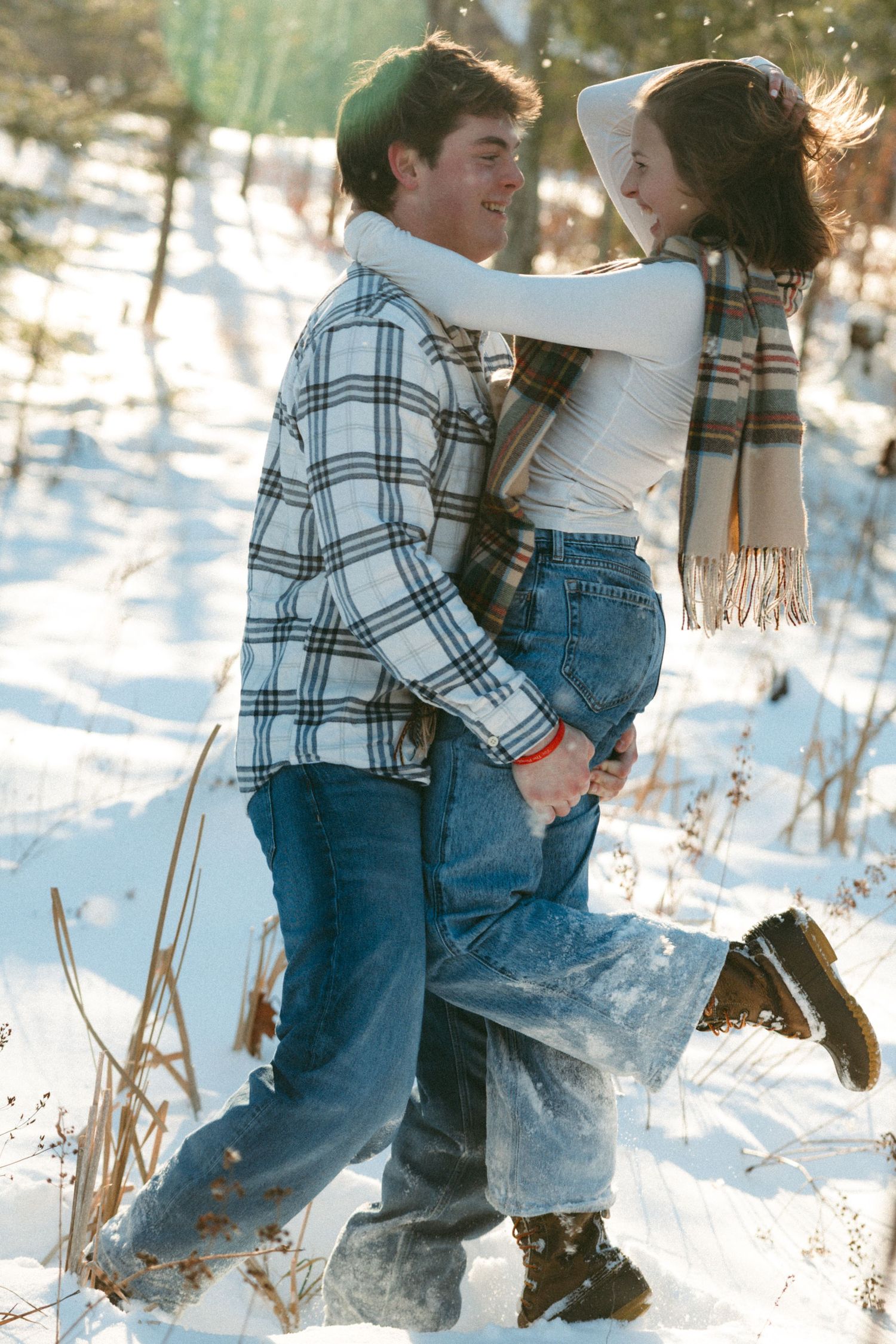 Two people in plaid shirts and overalls playing together in a snowy winter landscape.