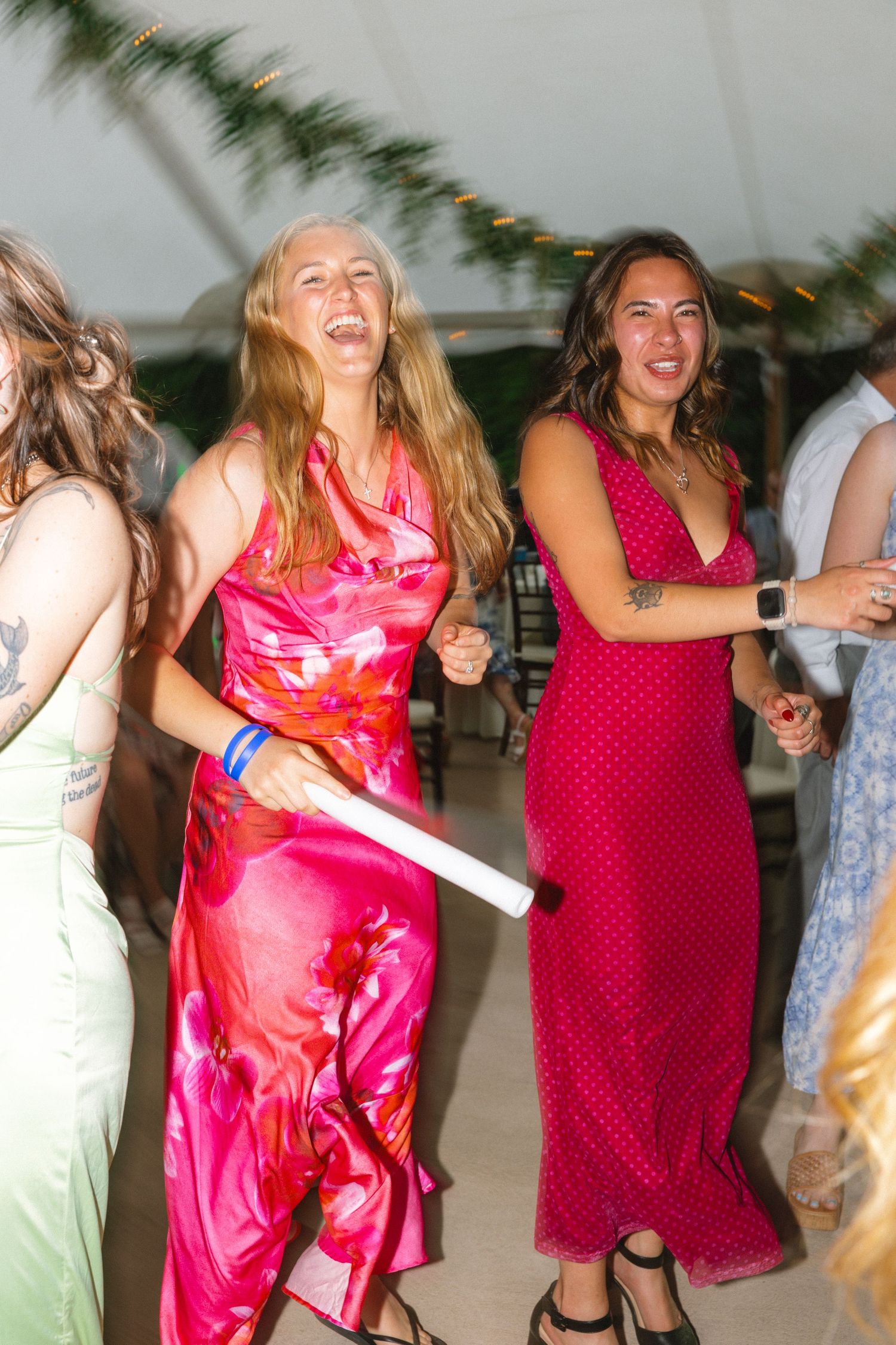 Two women in vibrant pink dresses laugh and dance joyfully at a lively wedding reception party.