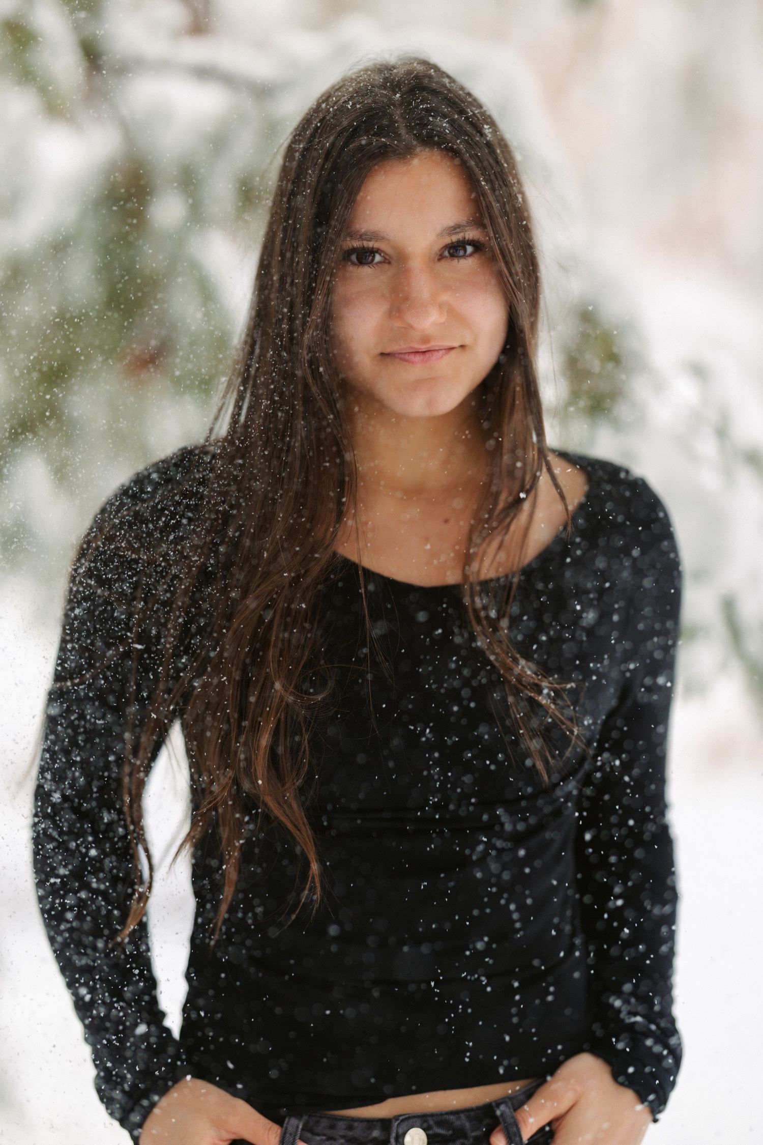 A woman in a black sweater poses in the snow while snowflakes fall around her creating a magical winter portrait.