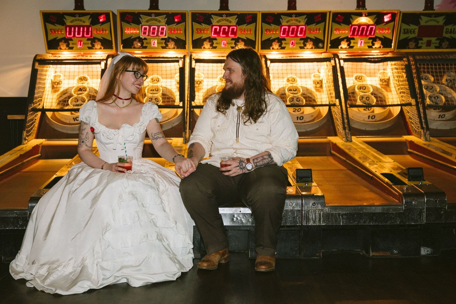 Bride and groom sitting together in front of arcade games, sharing a romantic moment at their unique wedding venue.