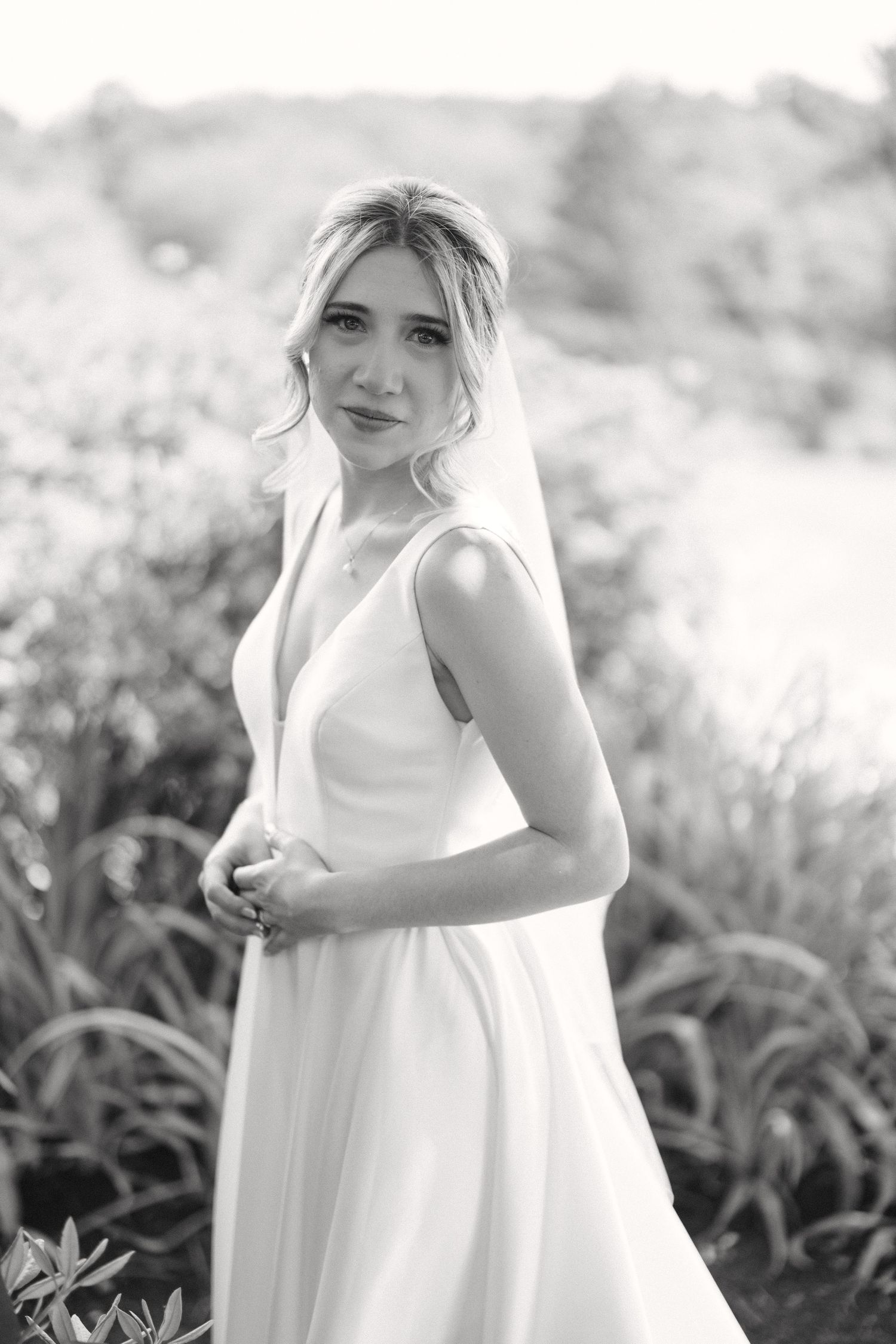 Black and white portrait of beautiful blonde bride in elegant gown with veil outdoors.