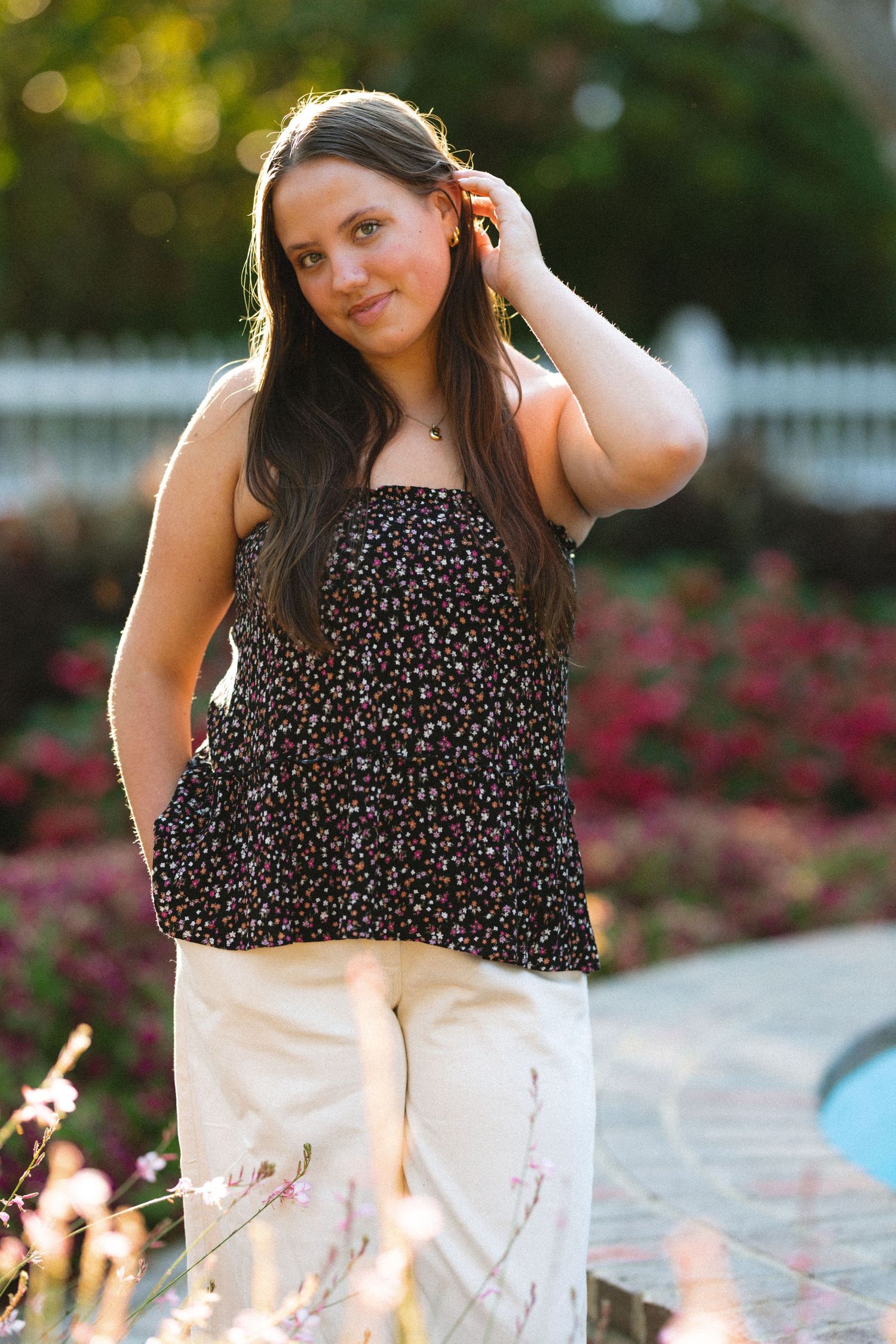 Summer senior session featuring floral top and white skirt against garden backdrop.