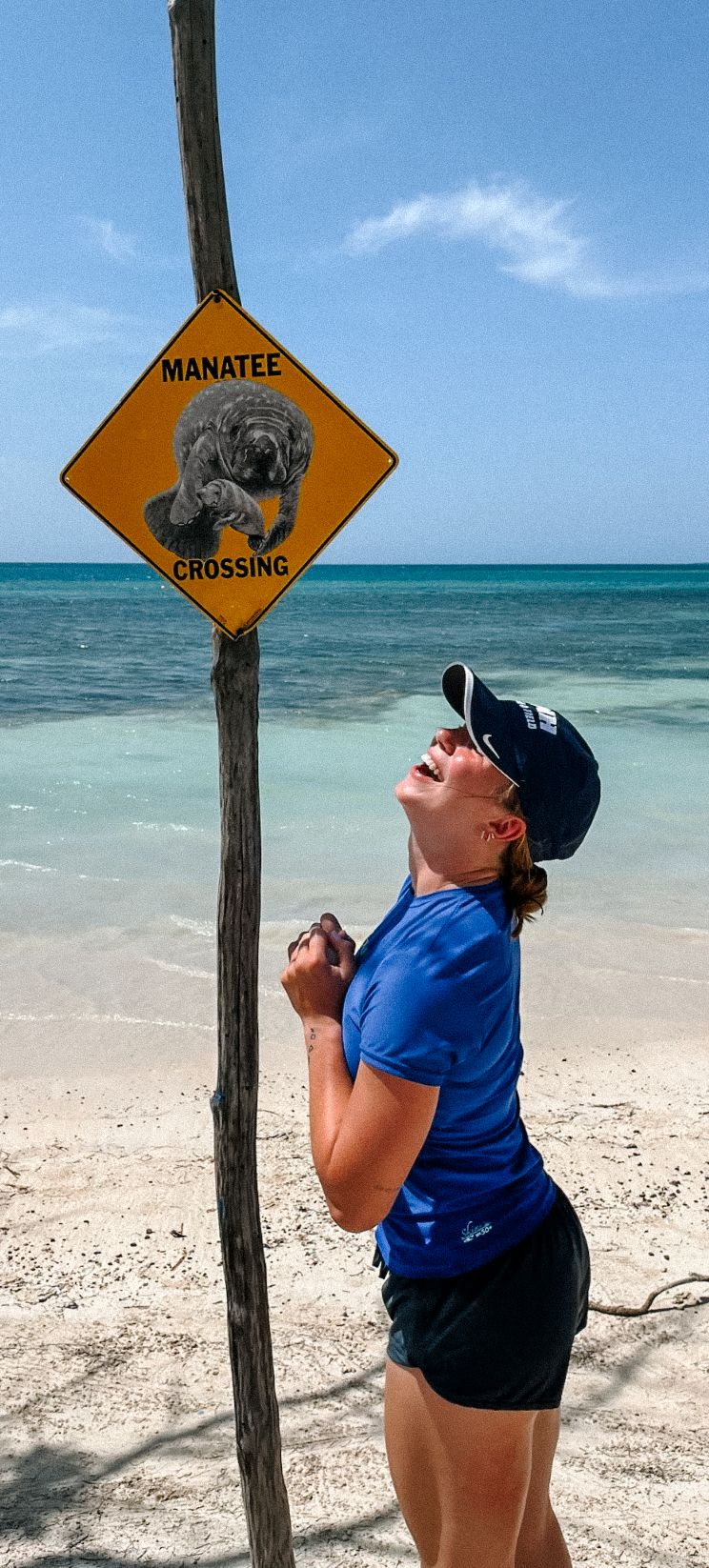 Playful poses by manatee crossing sign on tropical beach with turquoise waters.