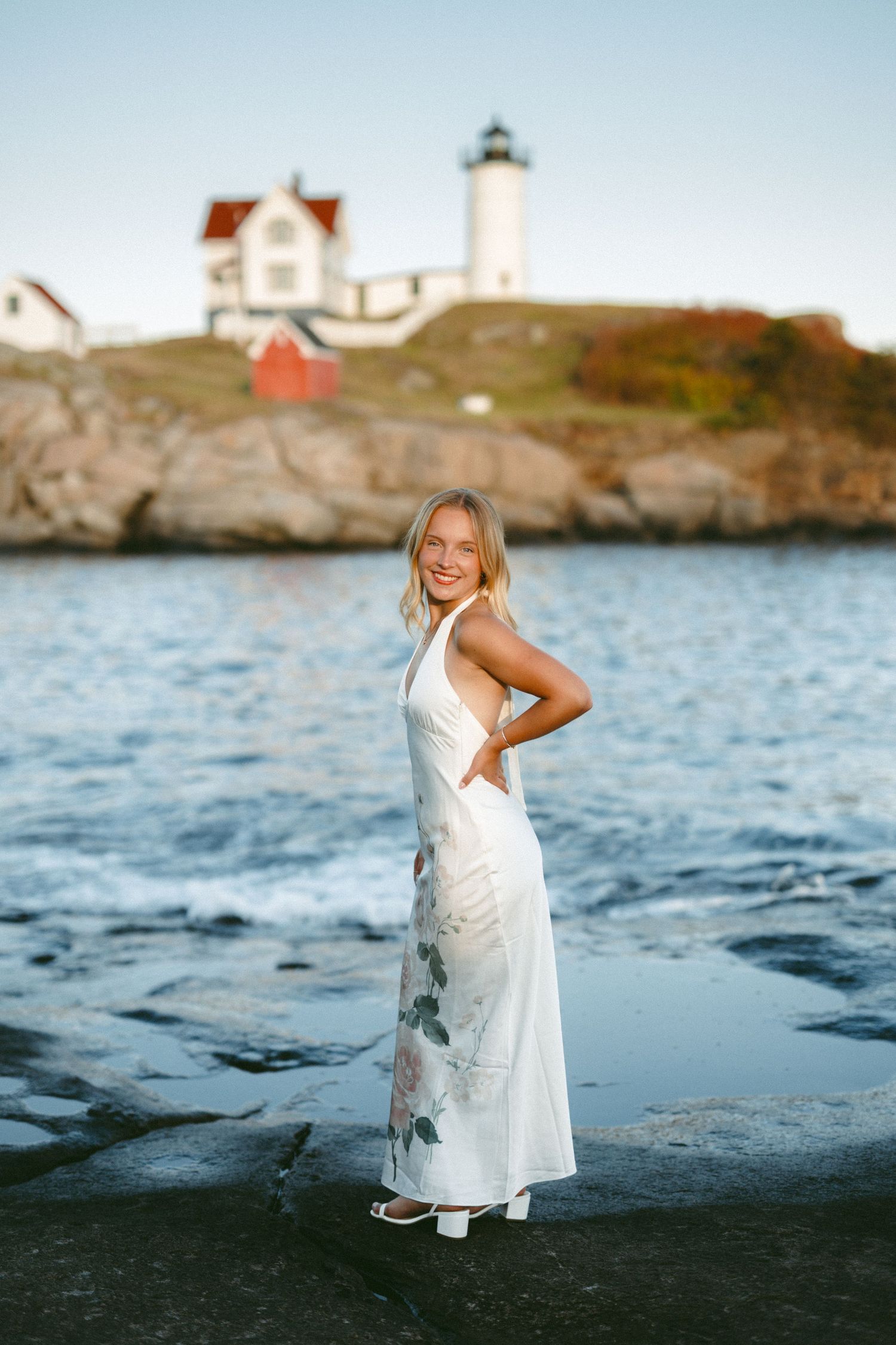 Coastal photoshoot with lighthouse and rocky shoreline in the background.