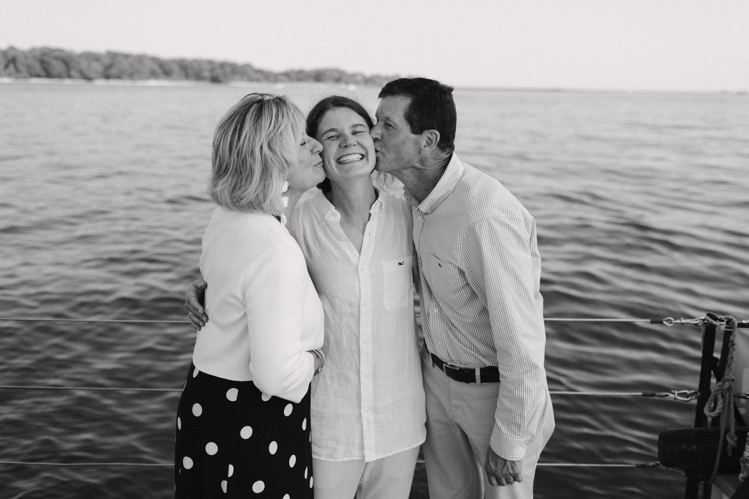 Three people sharing an affectionate moment on a boat with water in background.