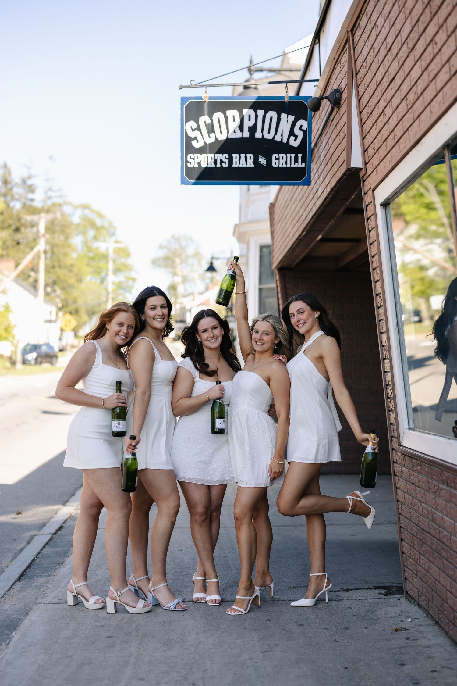 Group of graduates in white dresses pose together outside Scorpions sports bar.