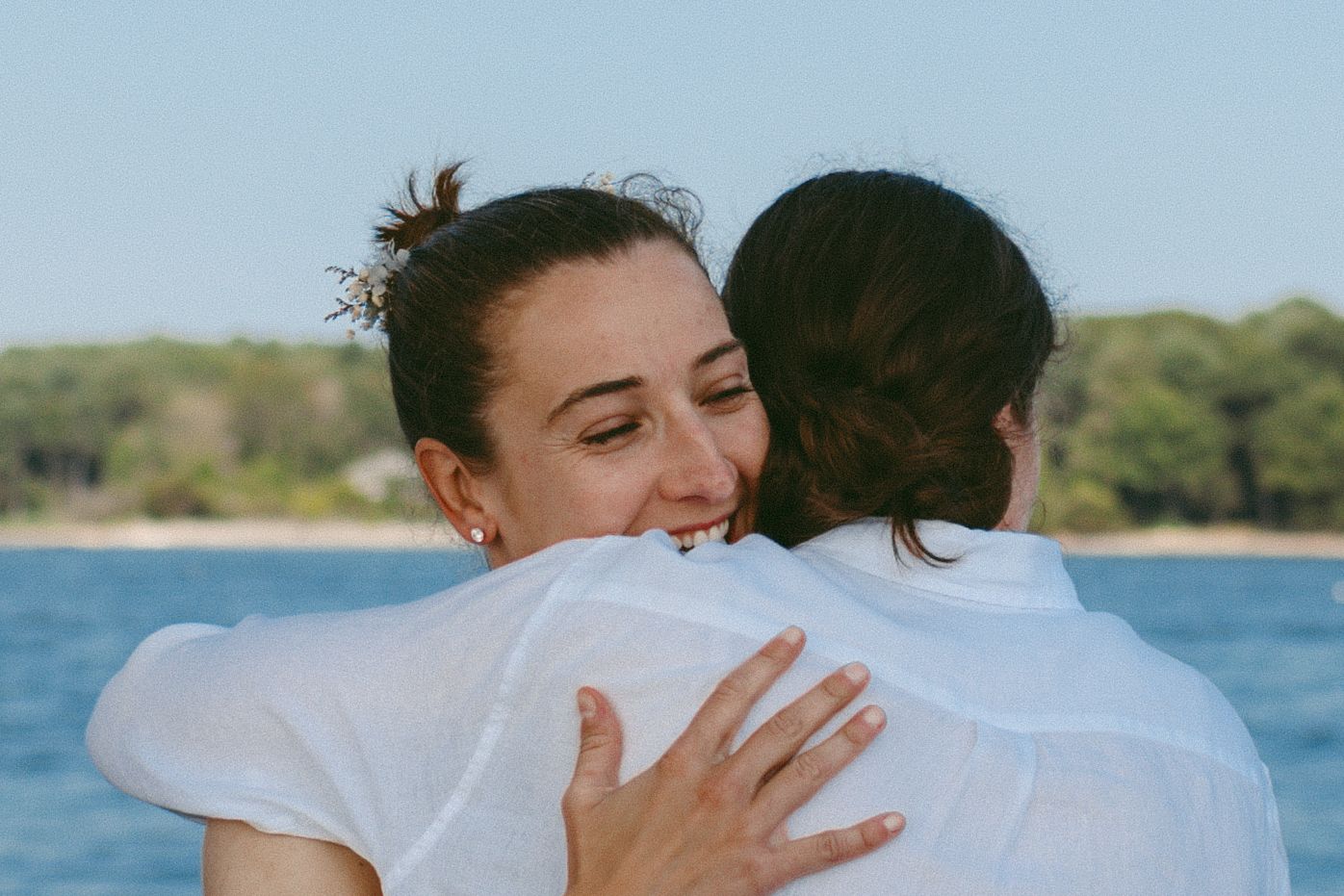 Two people share an emotional hug during a waterfront celebration.