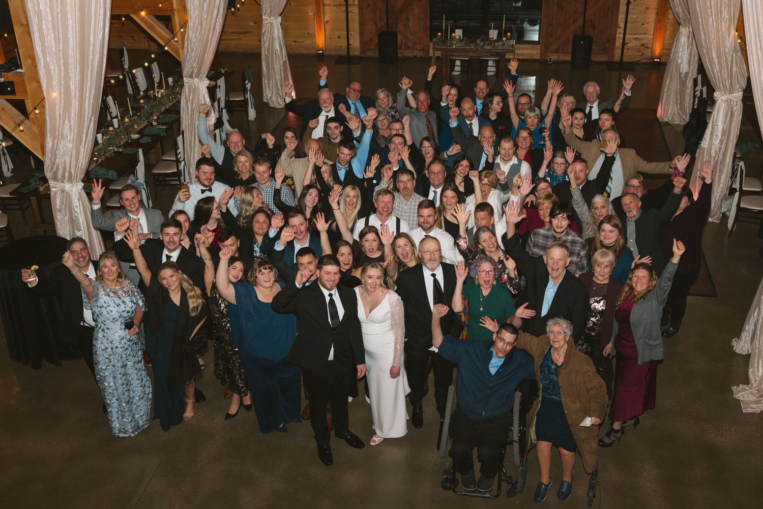 A large crowd of wedding guests dancing and celebrating together on a dimly lit dance floor at a reception.