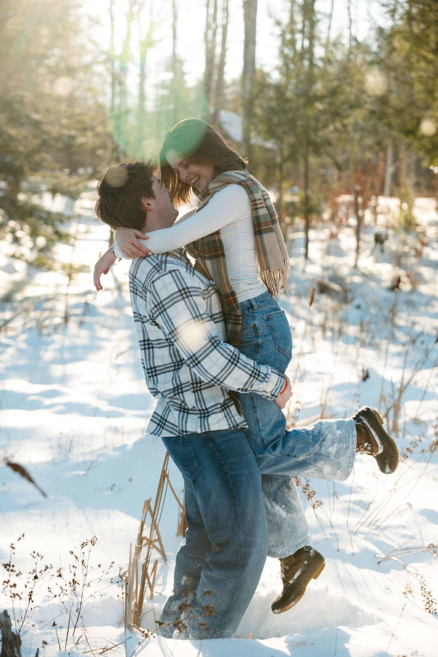 A romantic winter embrace between a couple in plaid and denim against a snowy forest backdrop.
