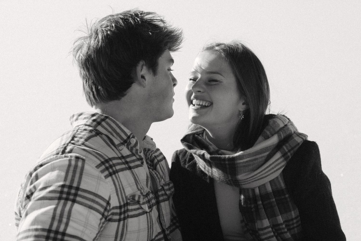 A black and white candid photo of two people laughing together while wearing plaid and scarves.