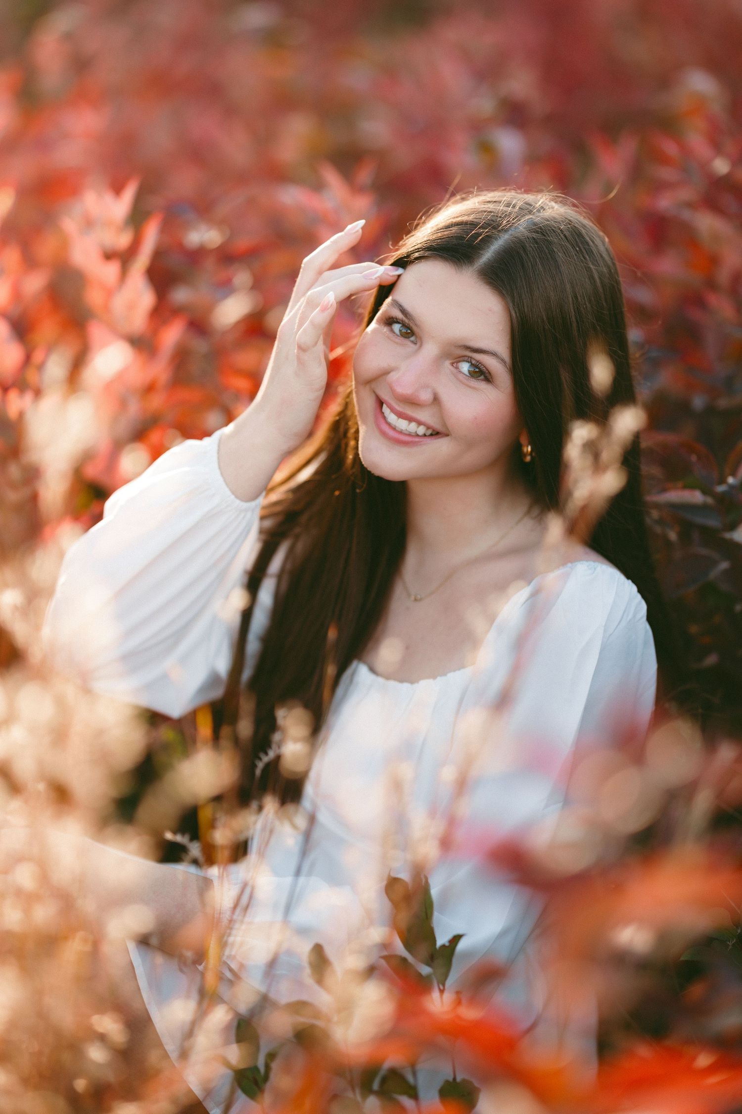 Senior through red autumn leaves with soft bokeh lighting effects.