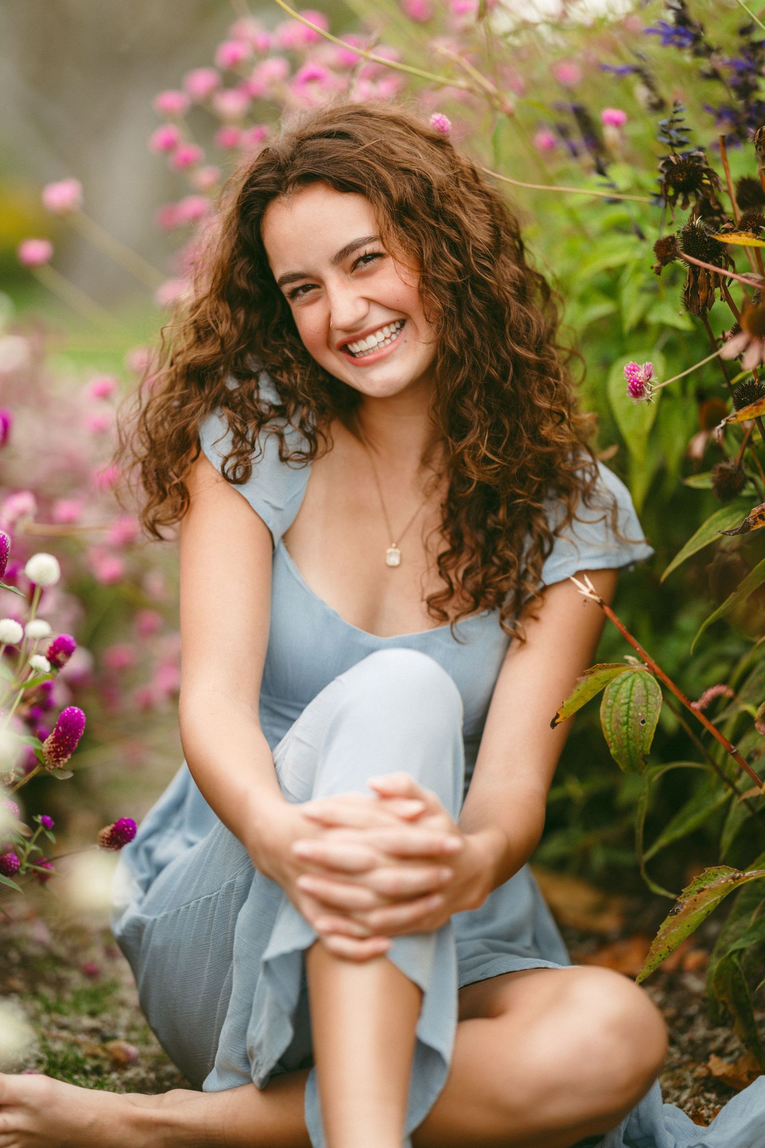 Soft pink flowers frame a portrait in a blue dress amid a garden setting.
